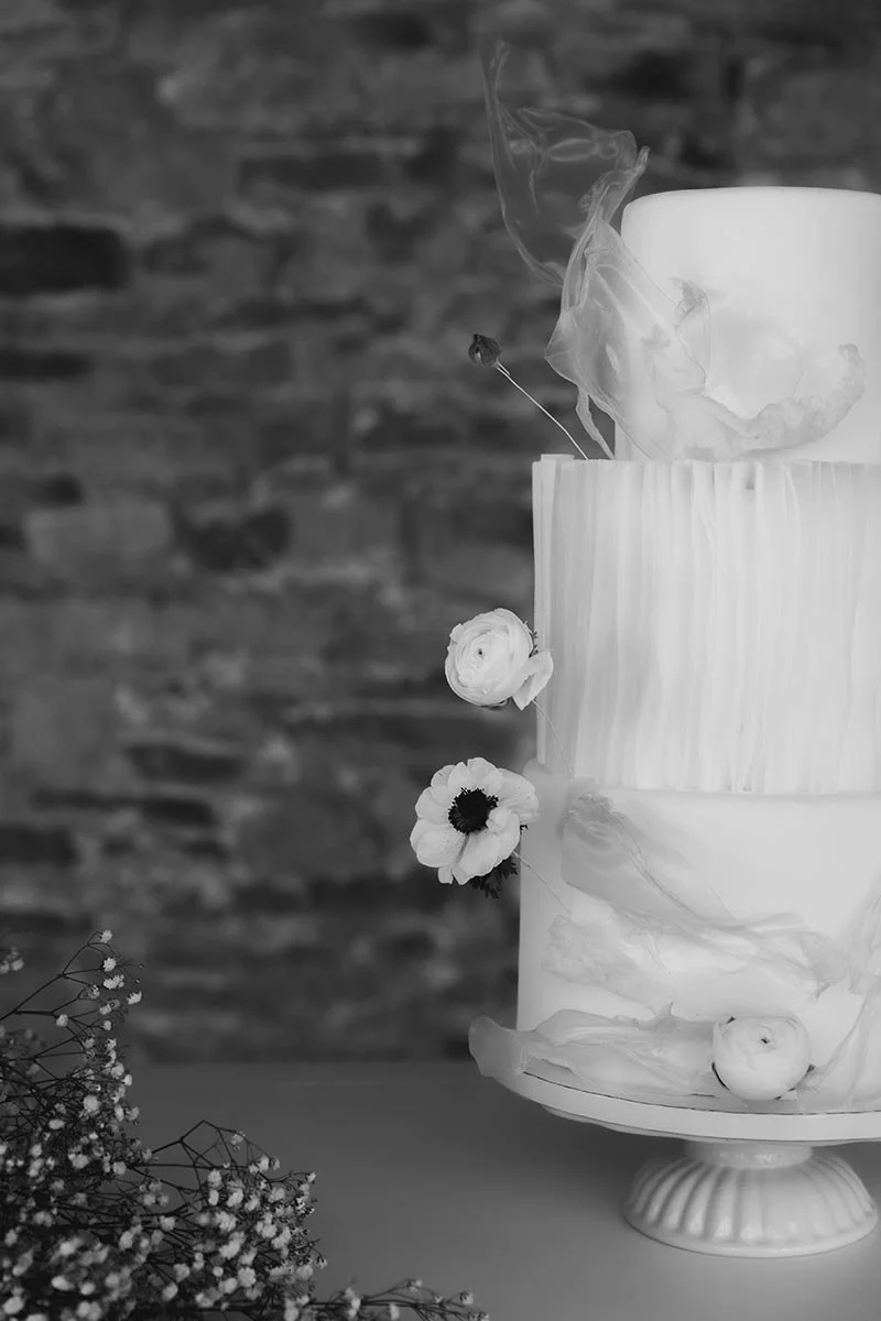 Schwarz-Weiß-Aufnahme einer modernen Hochzeitstorte mit floralen Details und aufsteigendem Rauch