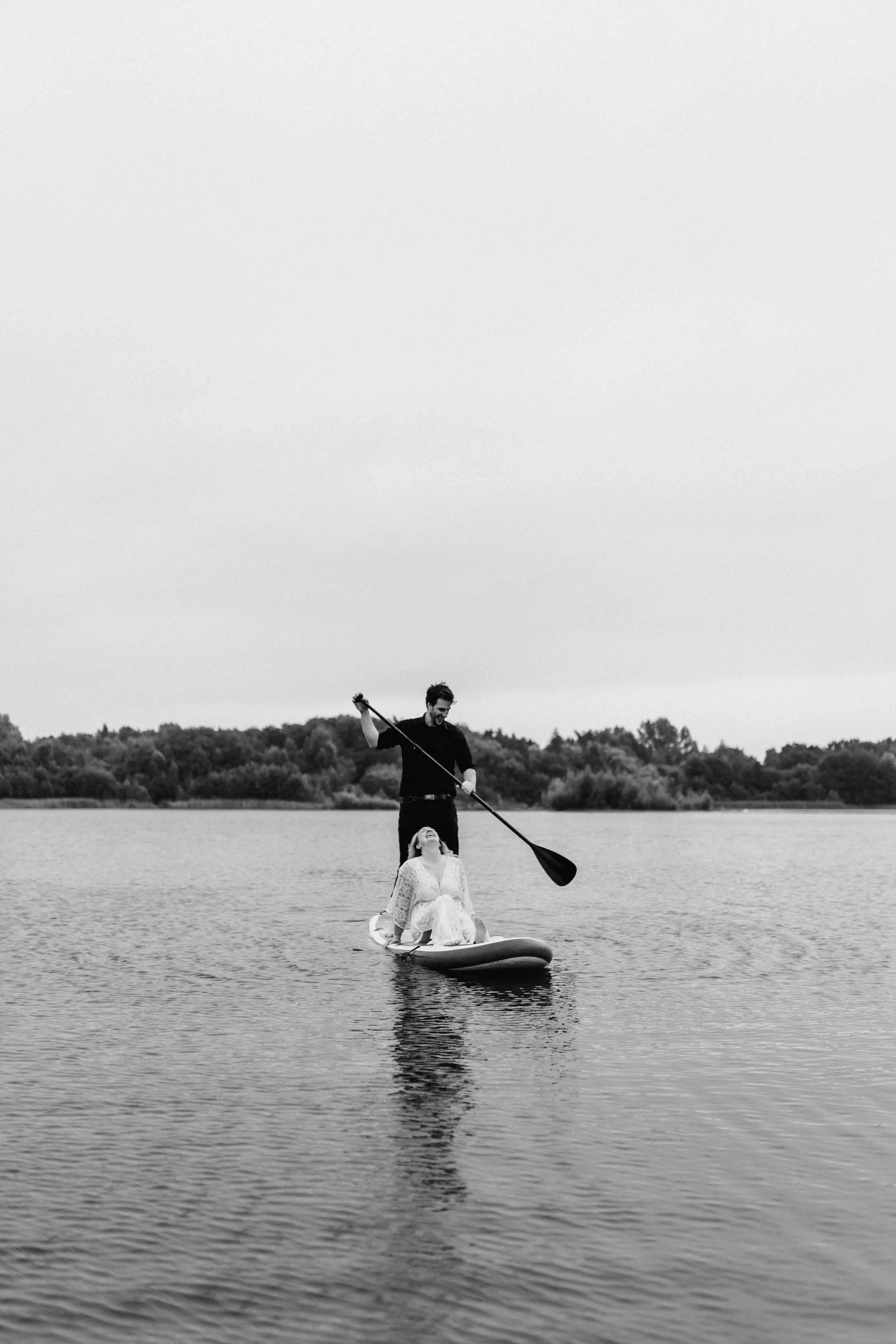 Schwarz-Weiß-Foto einer Person beim Stehpaddeln auf einem SUP-Board auf dem See