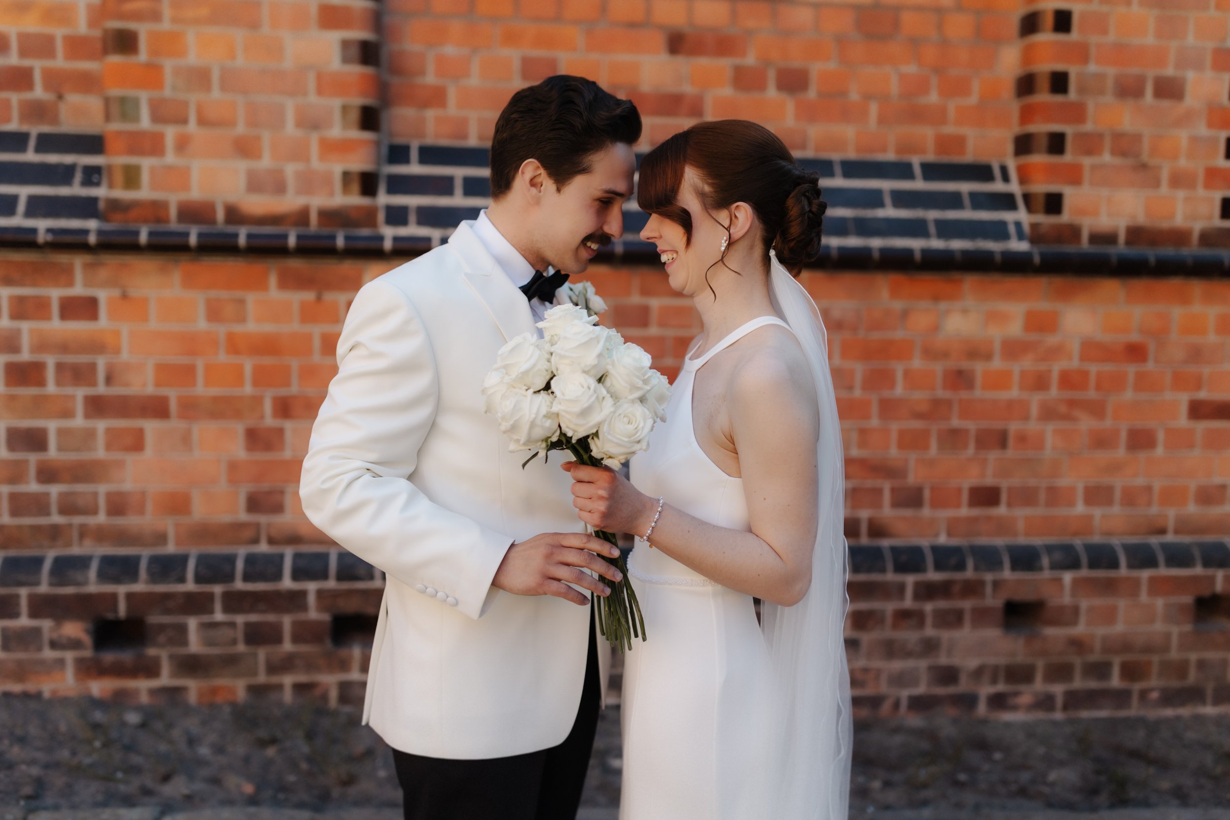 Lachendes Brautpaar mit weißem Brautstrauß bei seiner Hochzeit im Rathausgarten in Lüneburg.