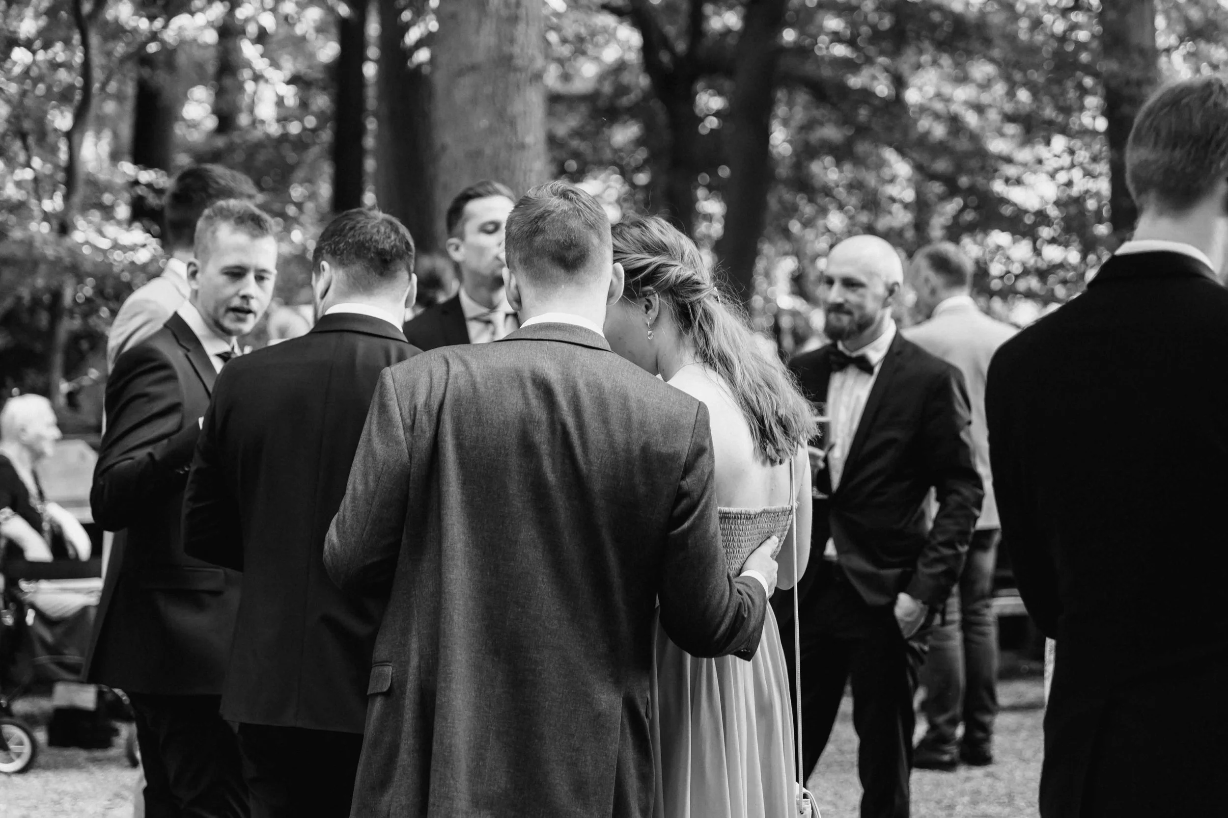 Schwarzweißaufnahme von Gästen in festlicher Kleidung beim Gespräch im Wald
