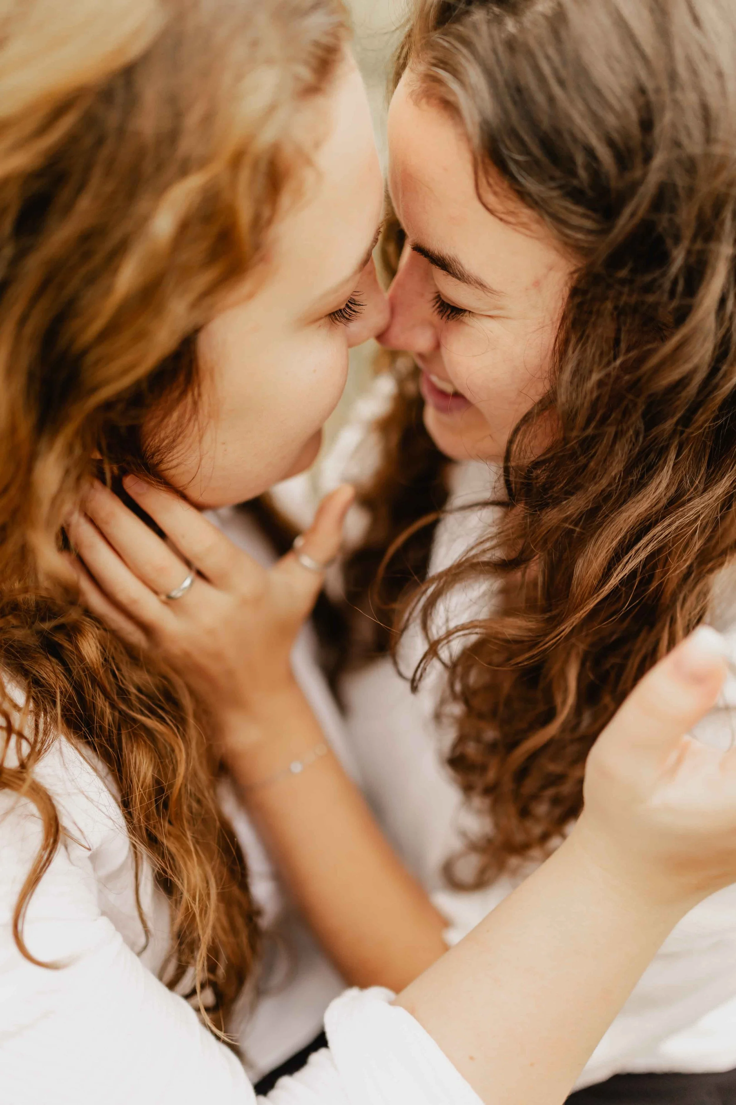 Zwei Frauen stehen eng beieinander, halten sich am Gesicht und schauen sich verliebt an, kurz vor einem Kuss