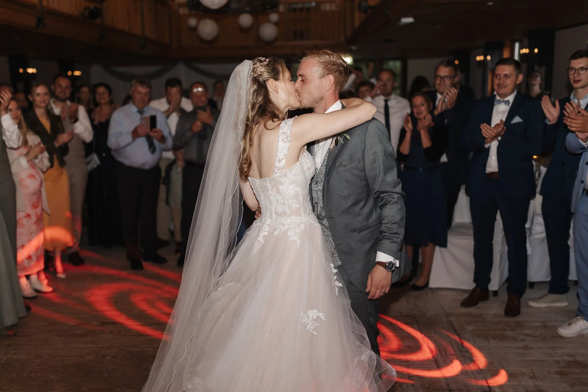 Brautpaar küsst sich beim Hochzeitstanz, während die Hochzeitsgäste applaudieren – Hochzeitsfeier im Heide Hotel Reinstorf bei Lüneburg.