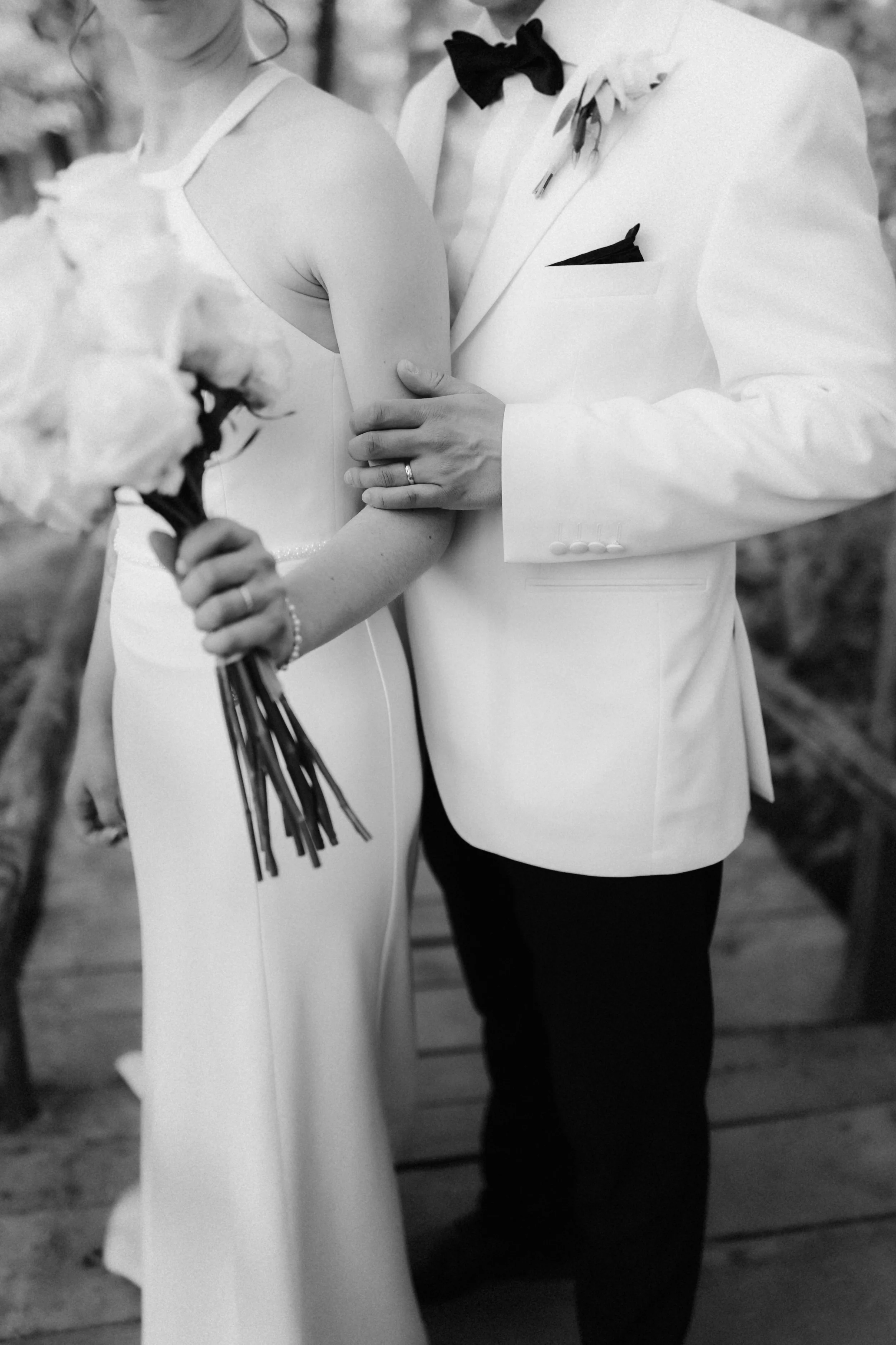 Romantische Schwarz-Weiß-Detailaufnahme eines Brautpaares bei einem Hochzeitsshooting in Lüneburg. Der Bräutigam hält liebevoll den Arm seiner Braut, die einen weißen Blumenstrauß trägt.