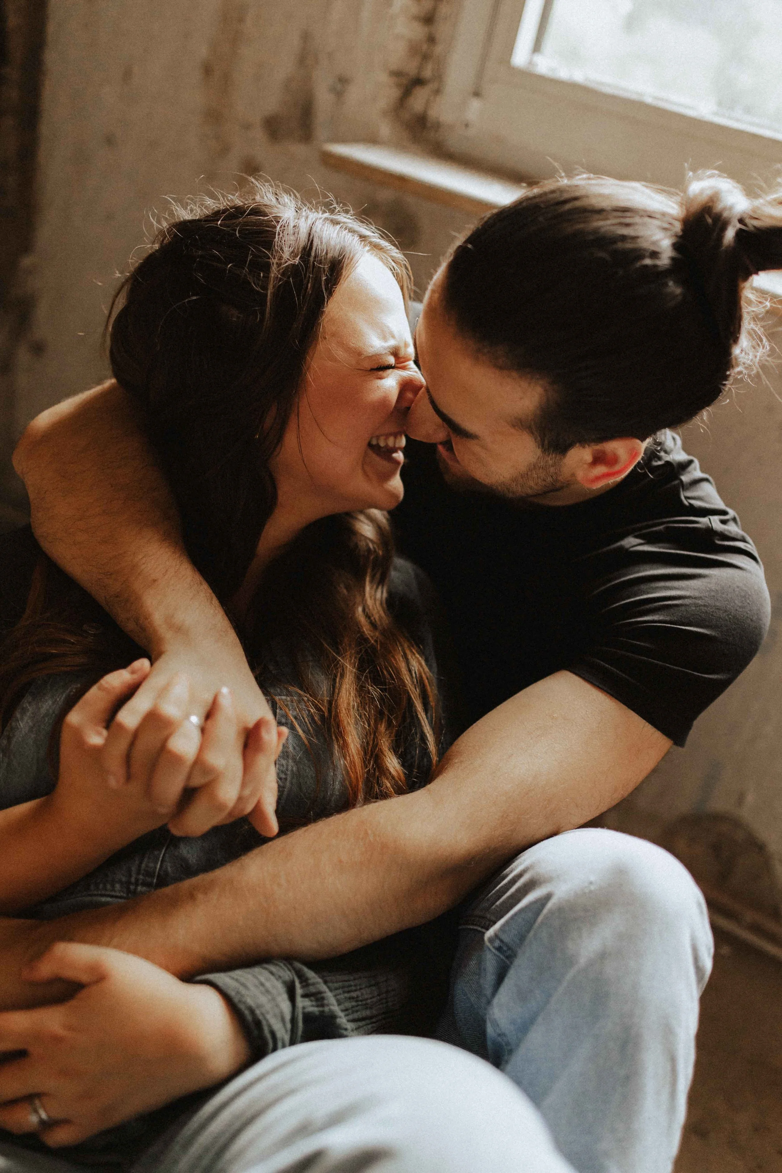 Paarshooting auf Baustelle – verliebtes Paar sitzt eng umschlungen am Fenster und lacht miteinander in Lüneburg.