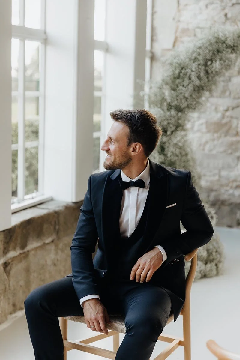 Bräutigam im schwarzen Anzug mit Fliege am Fenster – elegante Hochzeitsfotografie in Lüneburg