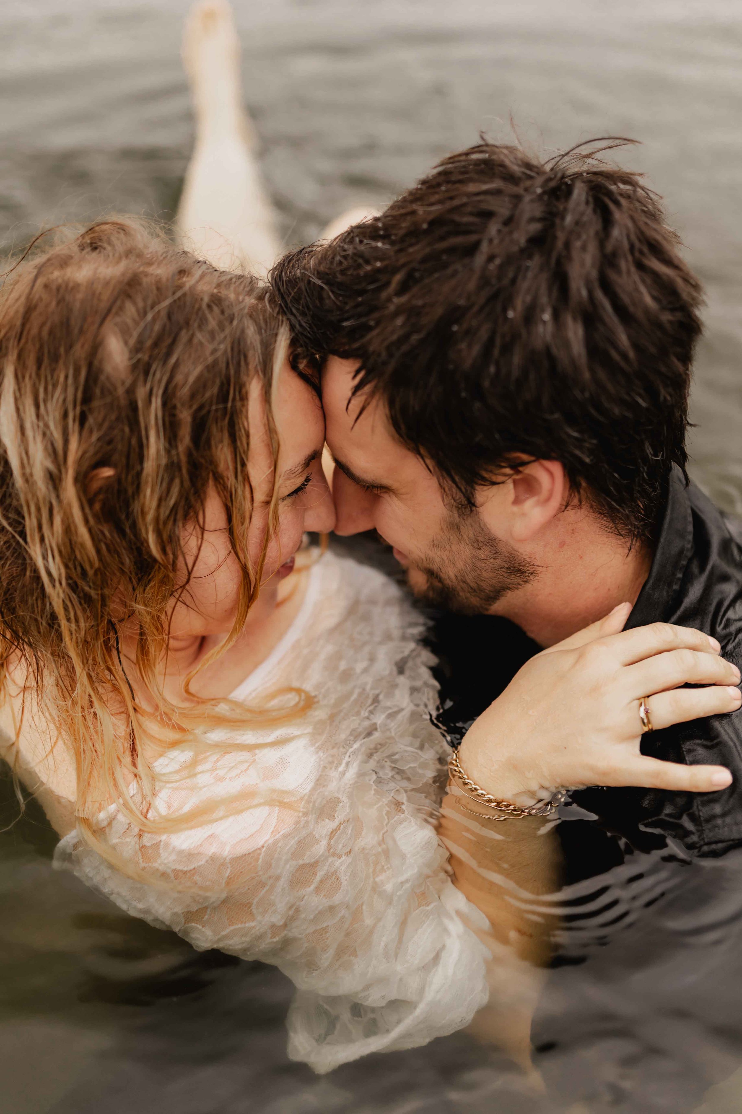 Paar steht eng umarmt im Wasser, legt die Stirn aneinander und lächelt vertraut