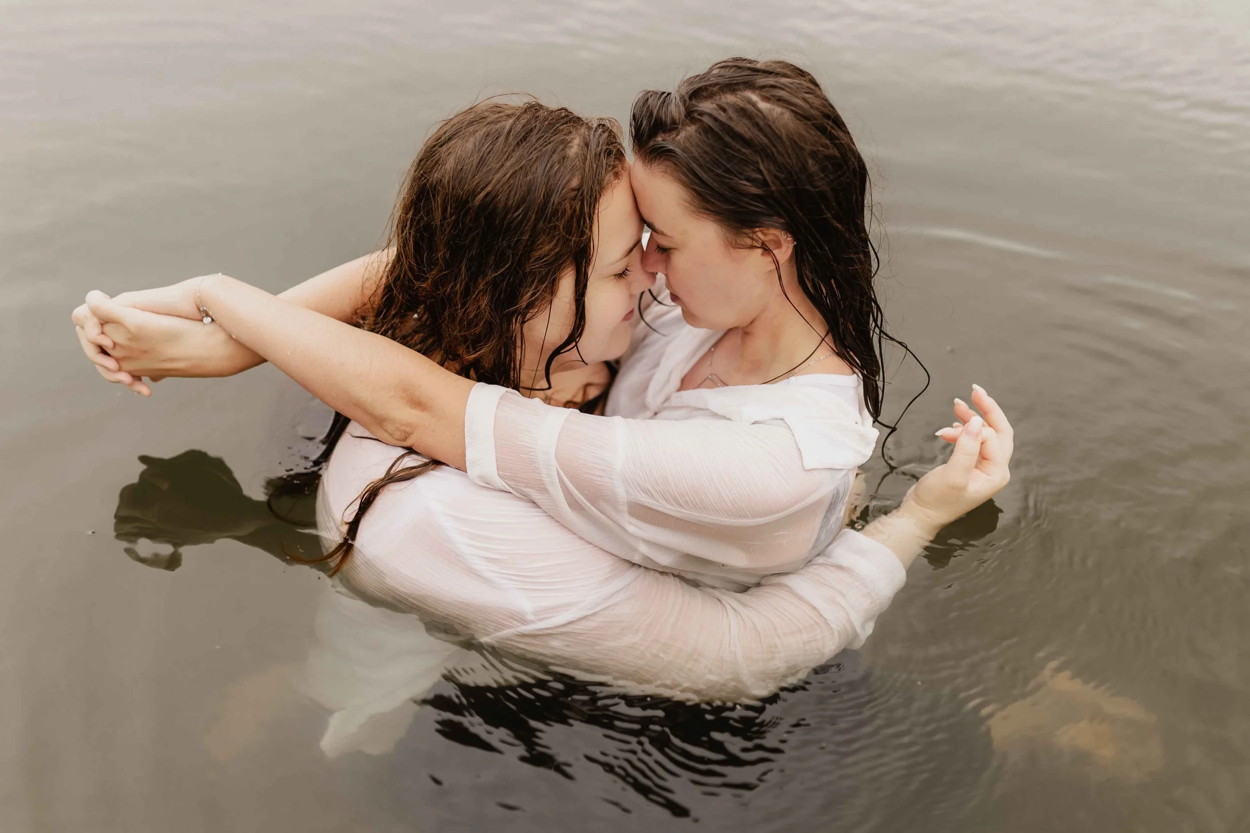 Zwei Frauen umarmen sich innig im Wasser, Stirn an Stirn, voller Zärtlichkeit