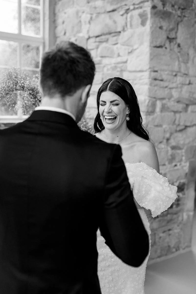 Lachende Braut beim emotionalen First Look mit ihrem Bräutigam in stilvoller Schwarz-Weiß-Fotografie