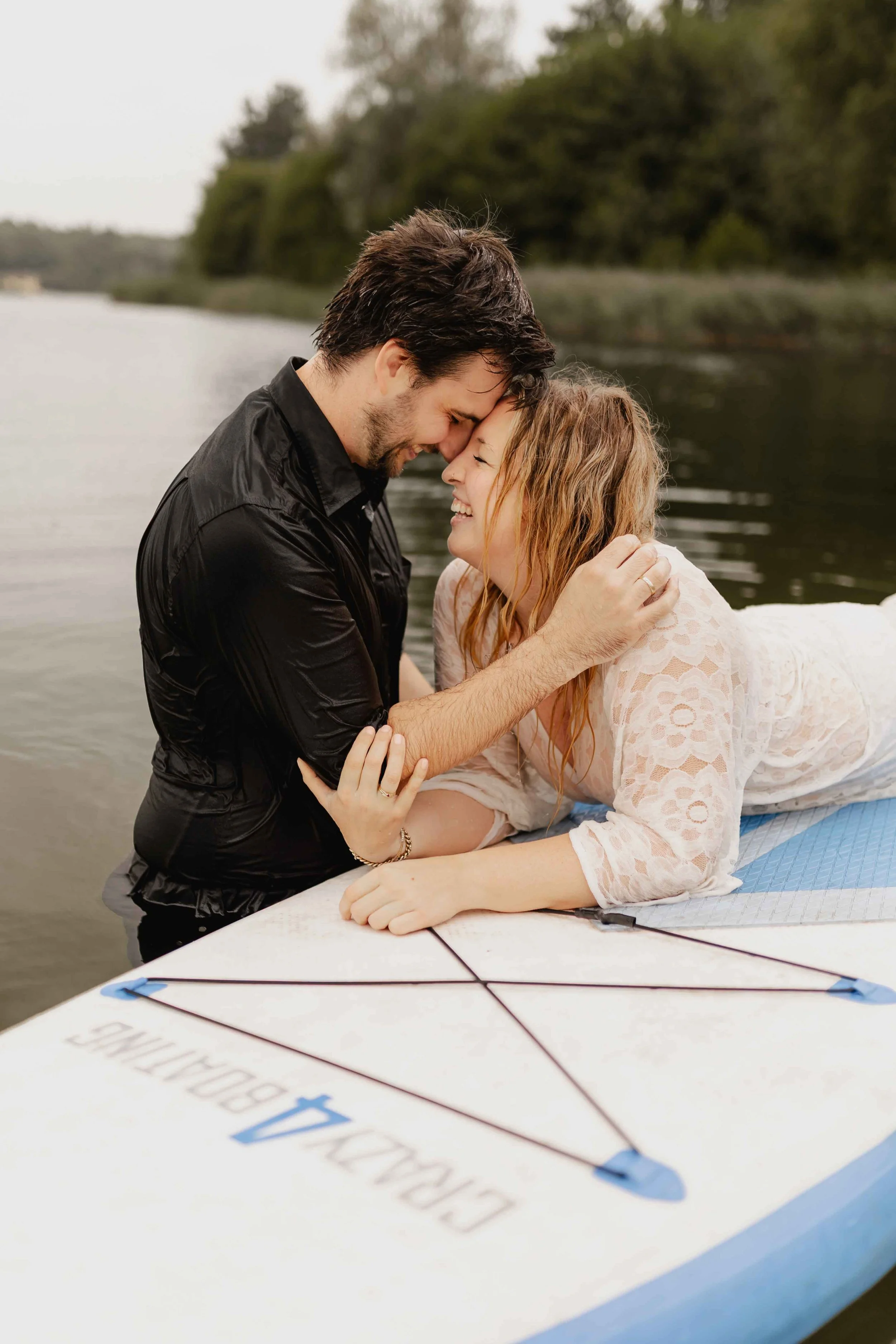 Paar lehnt Stirn an Stirn auf einem SUP-Board am See und hält sich liebevoll fest