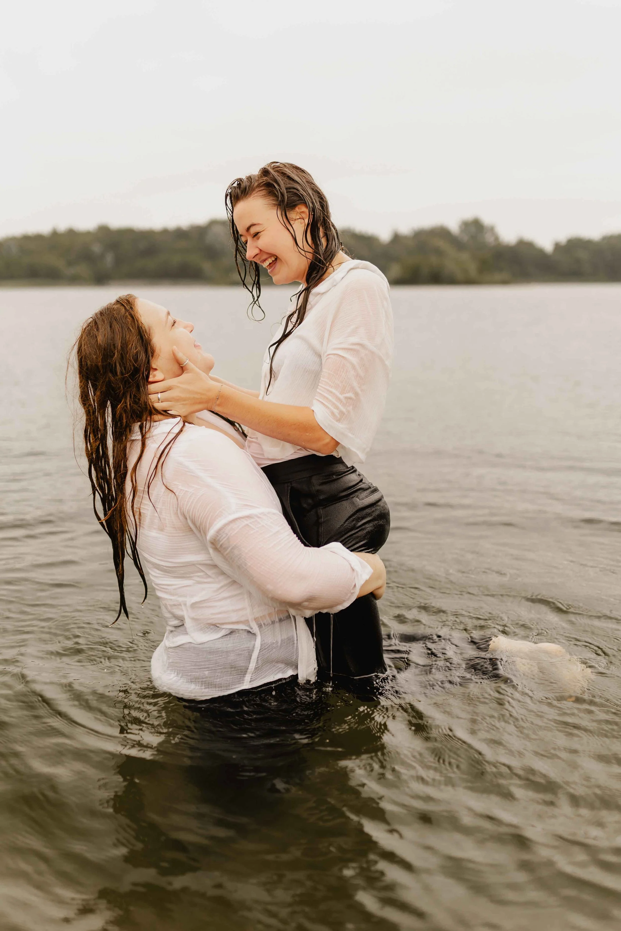 Zwei Frauen lachen und umarmen sich spielerisch im See, romantisches Paarshooting im Wasser