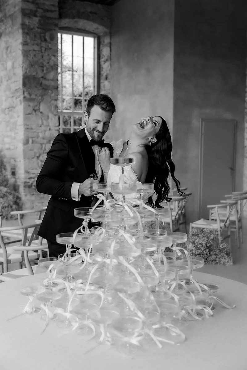 Schwarz-Weiß-Aufnahme eines lachenden Brautpaares beim Champagner – ein lebendiger, eleganter Moment einer modernen Hochzeitsreportage