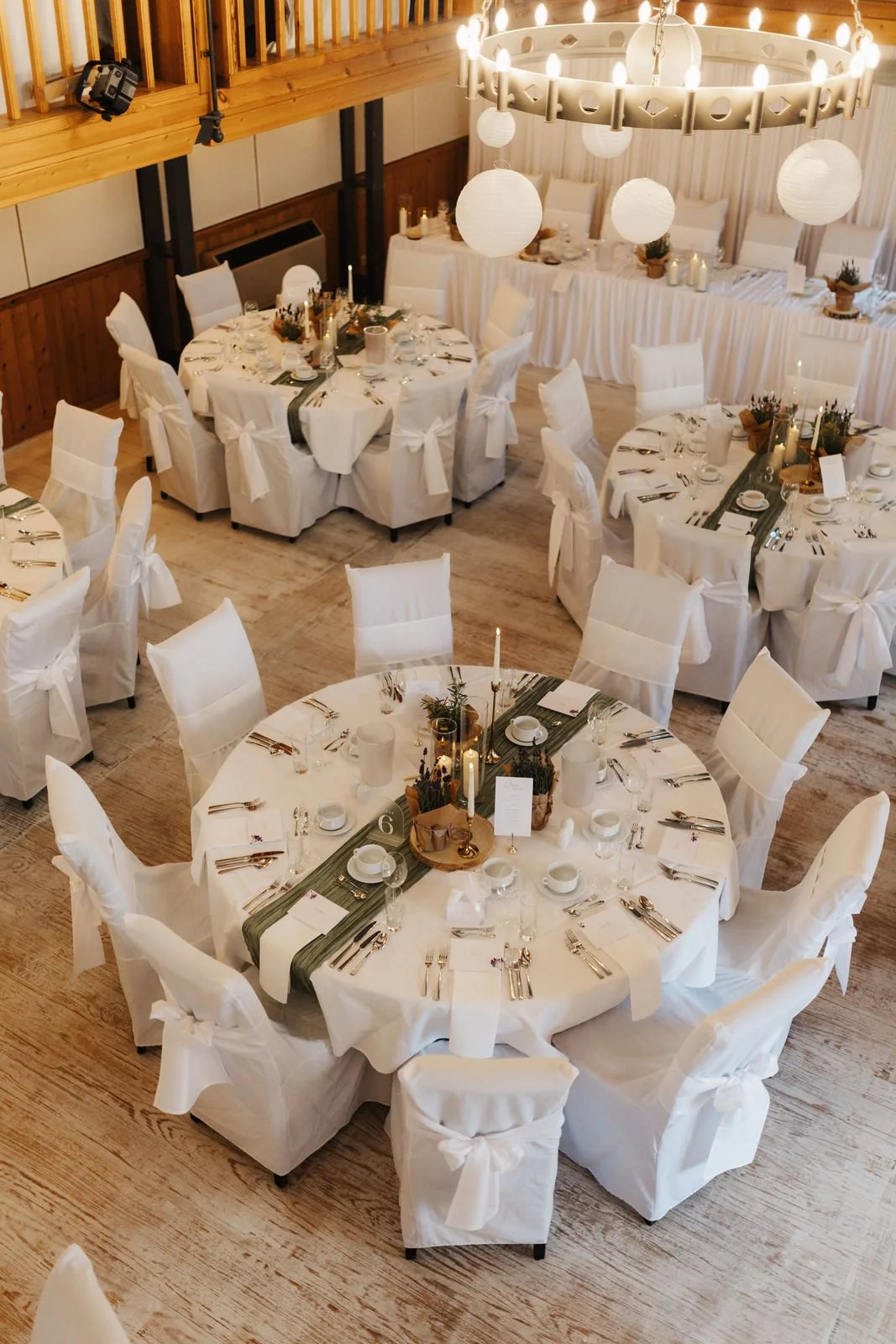 Festlich dekorierter Hochzeitssaal im Heide Hotel Reinstorf bei Lüneburg mit runden Gästetischen, weißen Stuhlhussen, grünen Tischläufern und modernen Kugelleuchten.