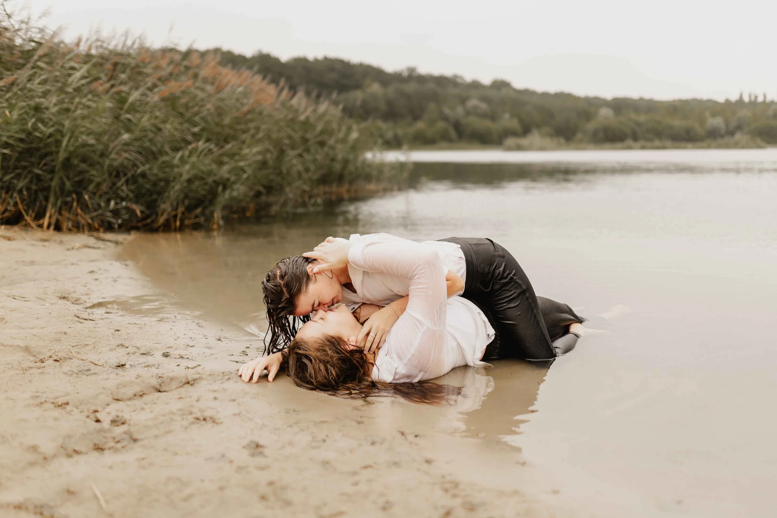 Zwei Frauen liegen eng umschlungen am Ufer des Sees im seichten Wasser und küssen sich innig
