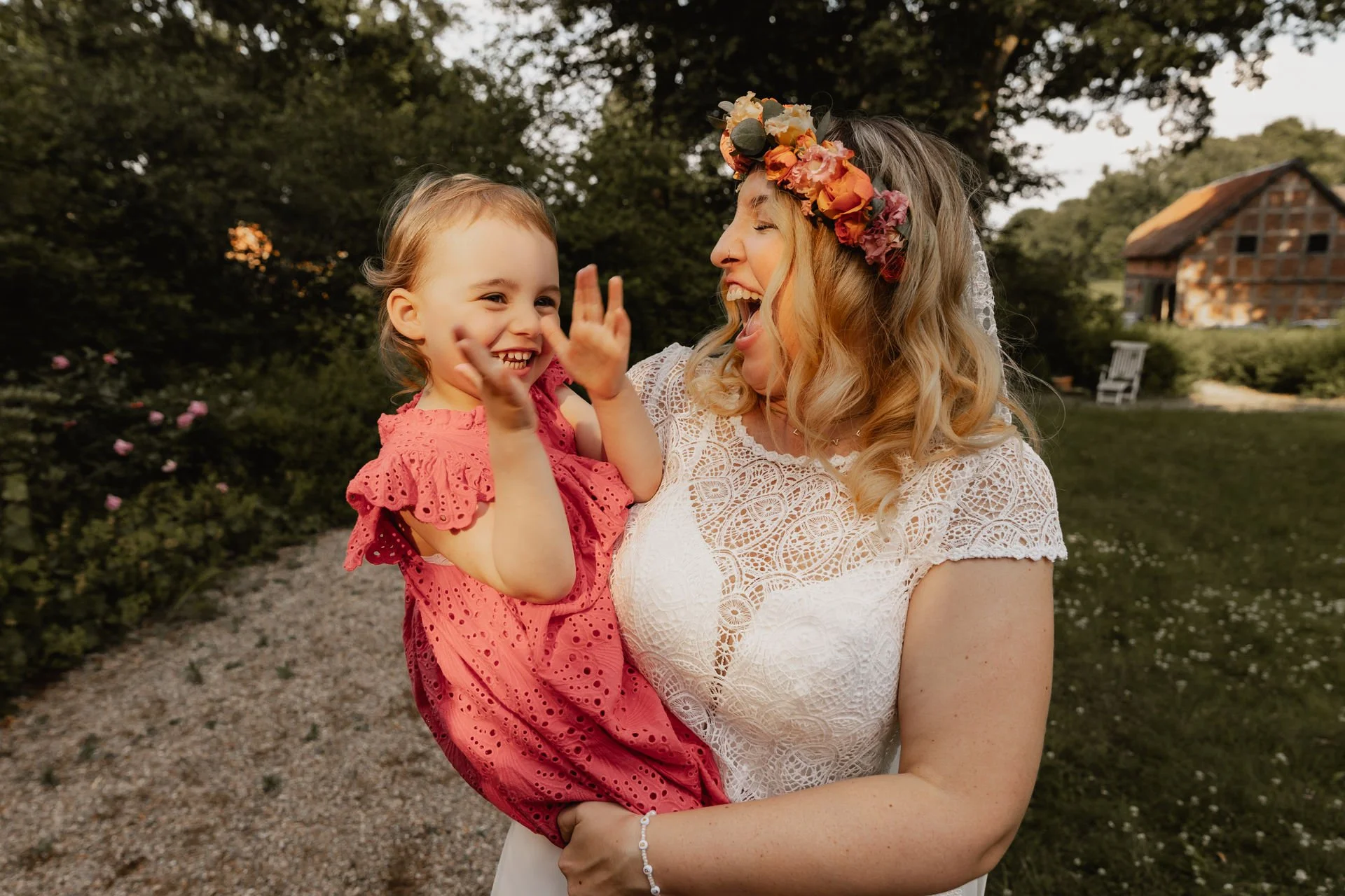 Lachende Braut mit Blumenkranz hält kleines Mädchen im Arm bei Sommerhochzeit in Lüneburg
