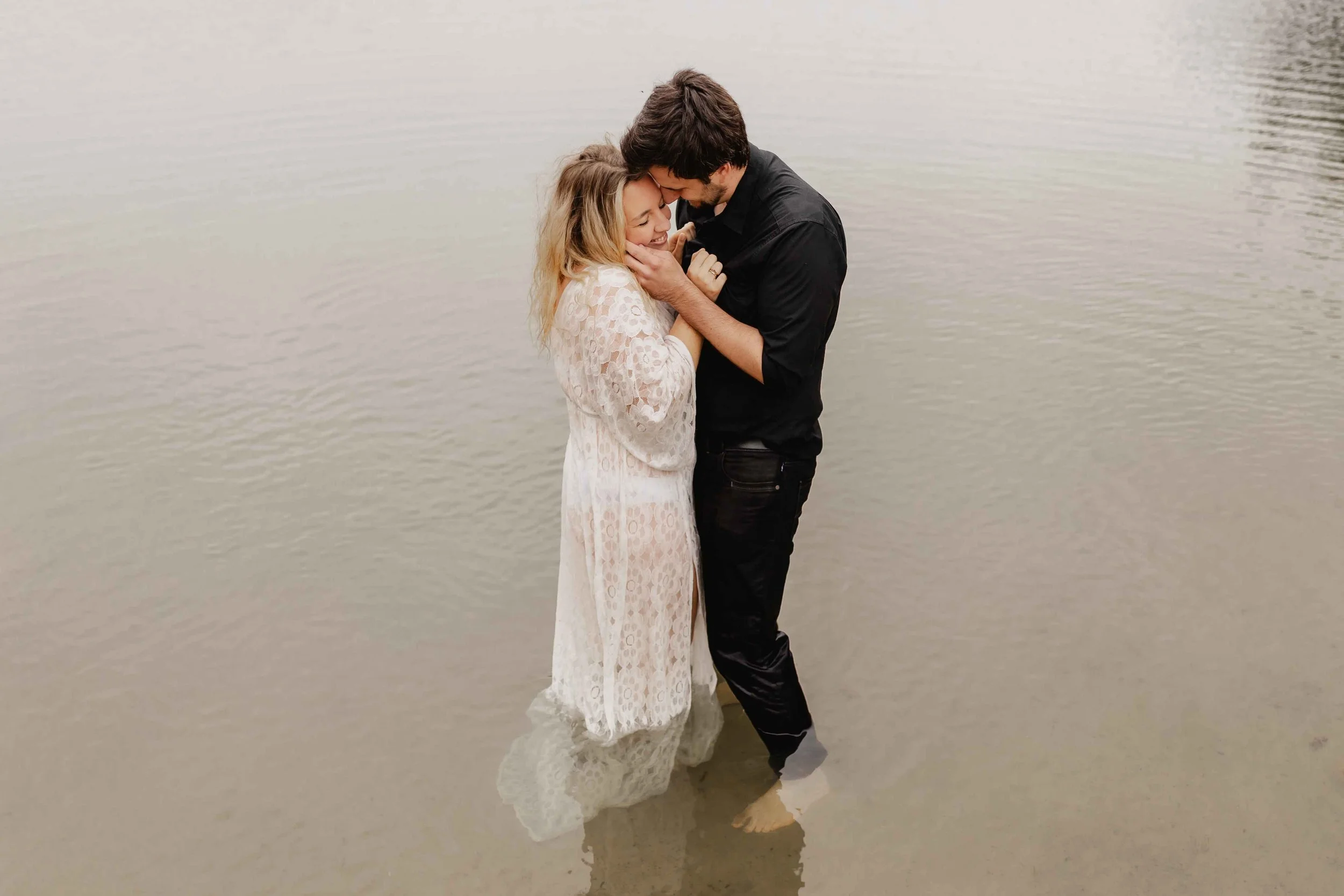 Paar steht barfuß im seichten Wasser und hält sich liebevoll Stirn an Stirn