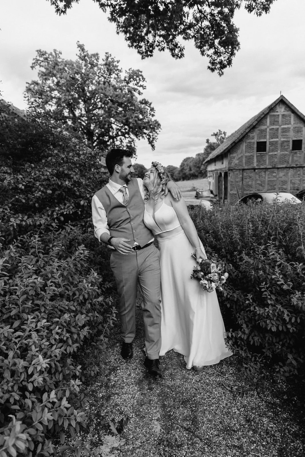 Brautpaar geht Hand in Hand über einen Gartenweg bei ihrer Hochzeit in Lüneburg in einer stilvollen Schwarzweißaufnahme