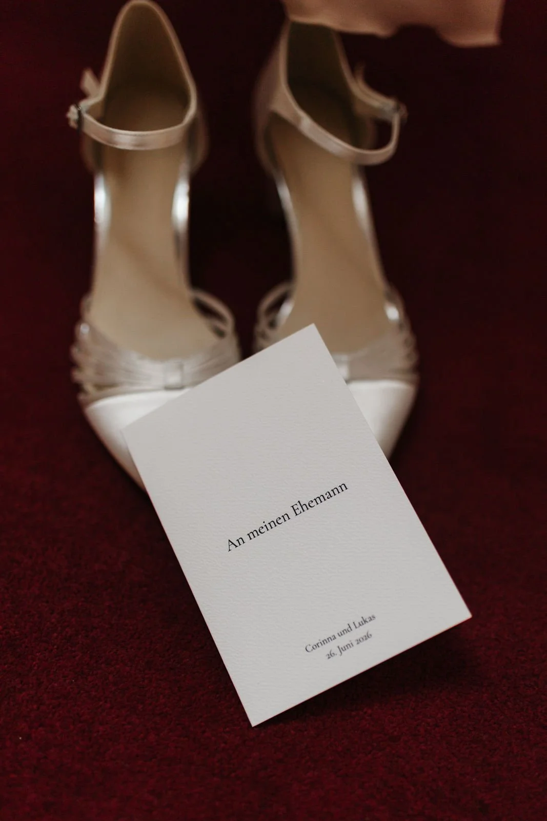 Elegante weiße Brautschuhe mit Riemchen und persönliche Hochzeitskarte „An meinen Ehemann“ als liebevoll arrangierte Hochzeitsdetails im Heide Hotel Reinstorf bei Lüneburg.