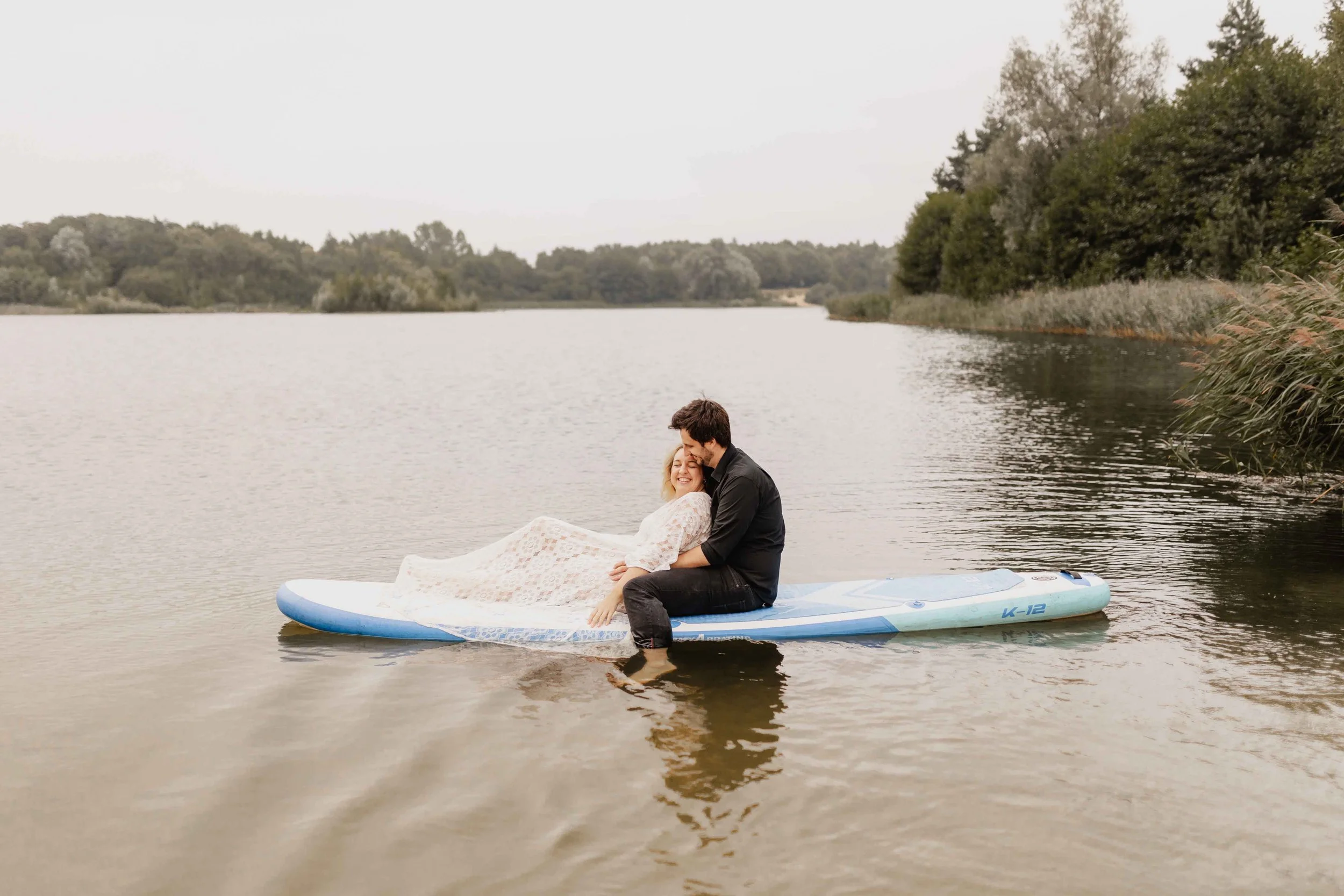 Paar sitzt eng umschlungen auf einem SUP-Board auf dem See, romantische Stimmung in der Natur