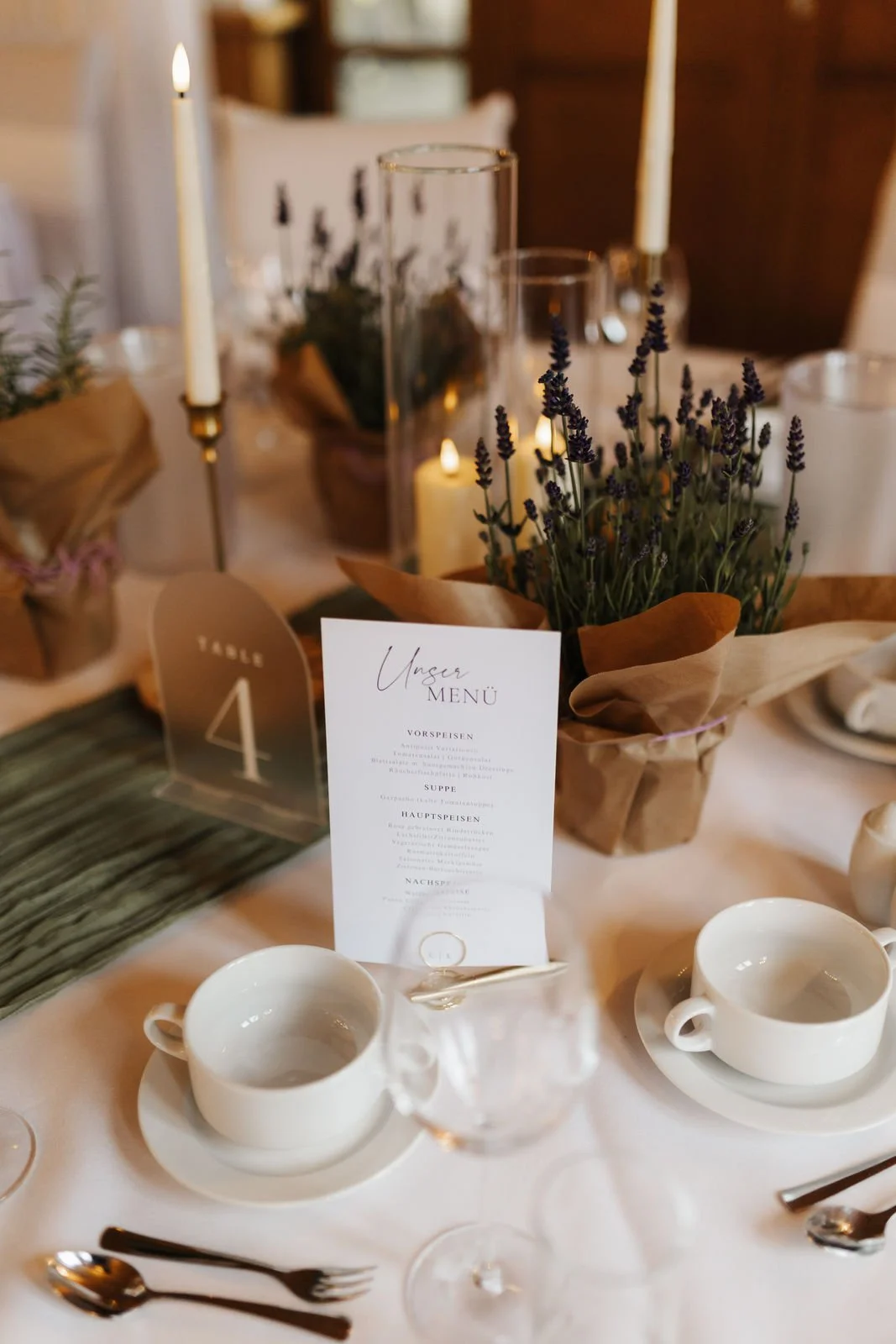 Stilvolle Hochzeitsdekoration im Heide Hotel Reinstorf bei Lüneburg mit Lavendel, brennenden Kerzen, Menükarte und Tischnummer auf einer festlich gedeckten Tafel.