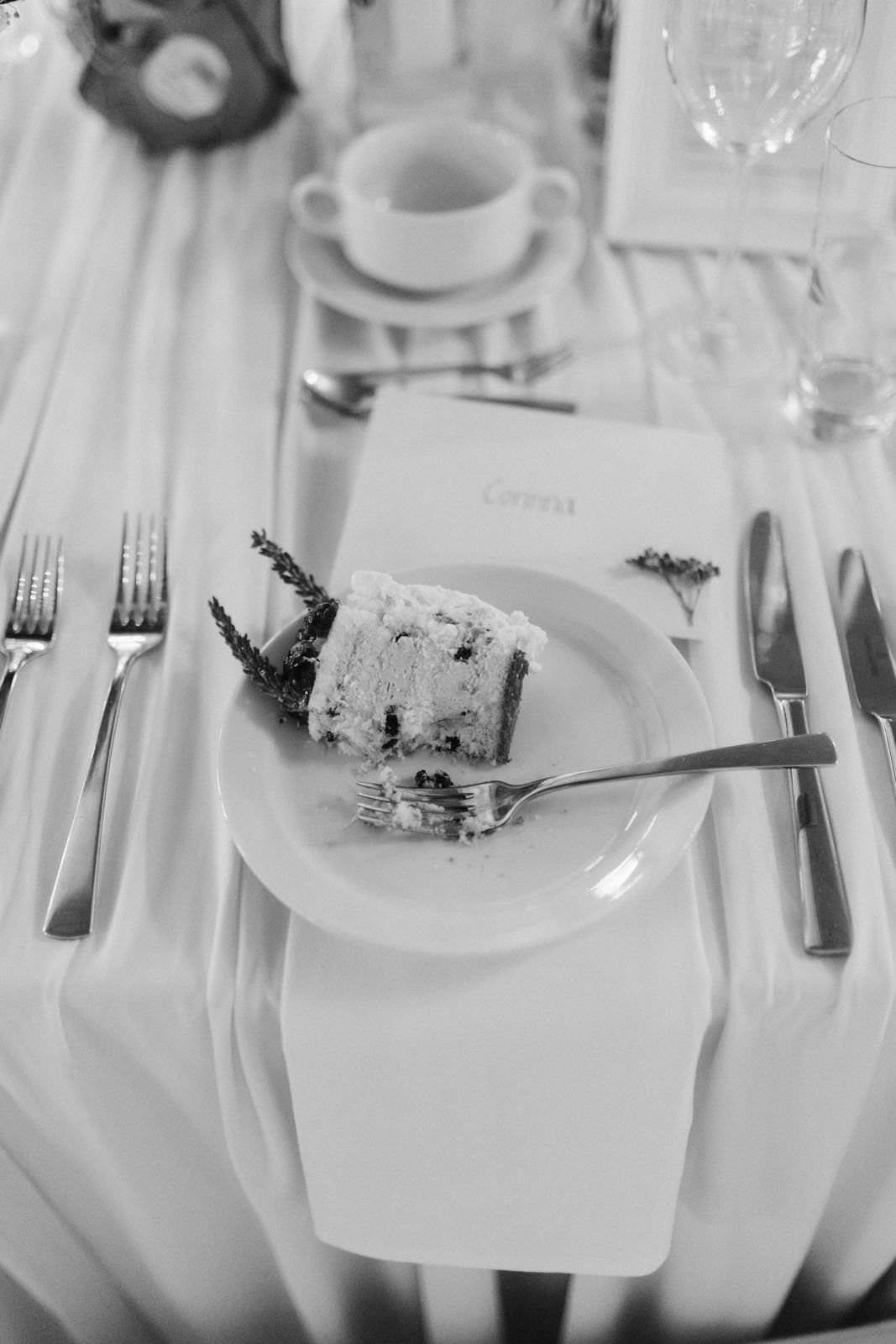 Stück Hochzeitstorte mit Lavendeldekoration auf einem festlich gedeckten Tisch im Heide Hotel Reinstorf bei Lüneburg – stilvolle Schwarz-Weiß-Detailaufnahme einer Hochzeitsreportage.