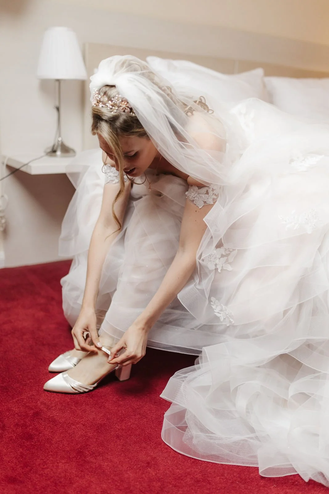 Braut zieht beim Getting Ready im Heide Hotel Reinstorf bei Lüneburg ihre eleganten Brautschuhe an. Ihr voluminöses Hochzeitskleid aus Tüll und der lange Schleier umrahmen den natürlichen Moment vor der Hochzeit.