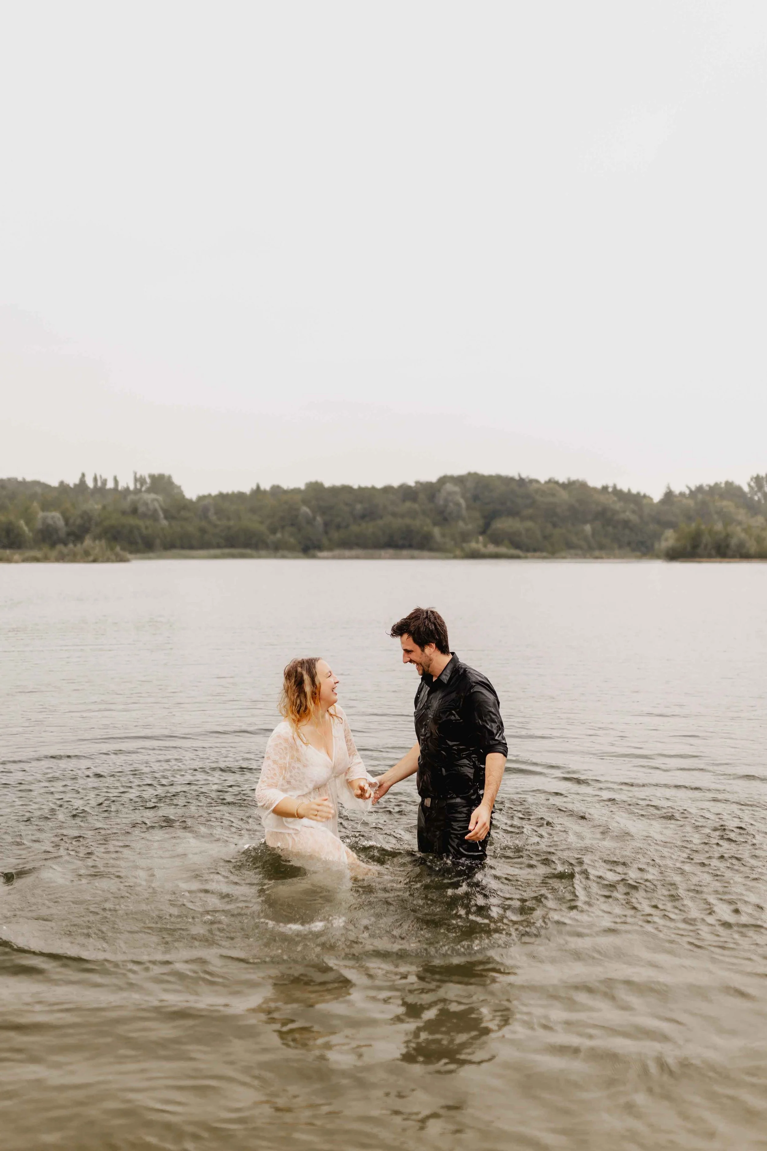 Paar steht im Wasser, hält sich an den Händen und lächelt einander an