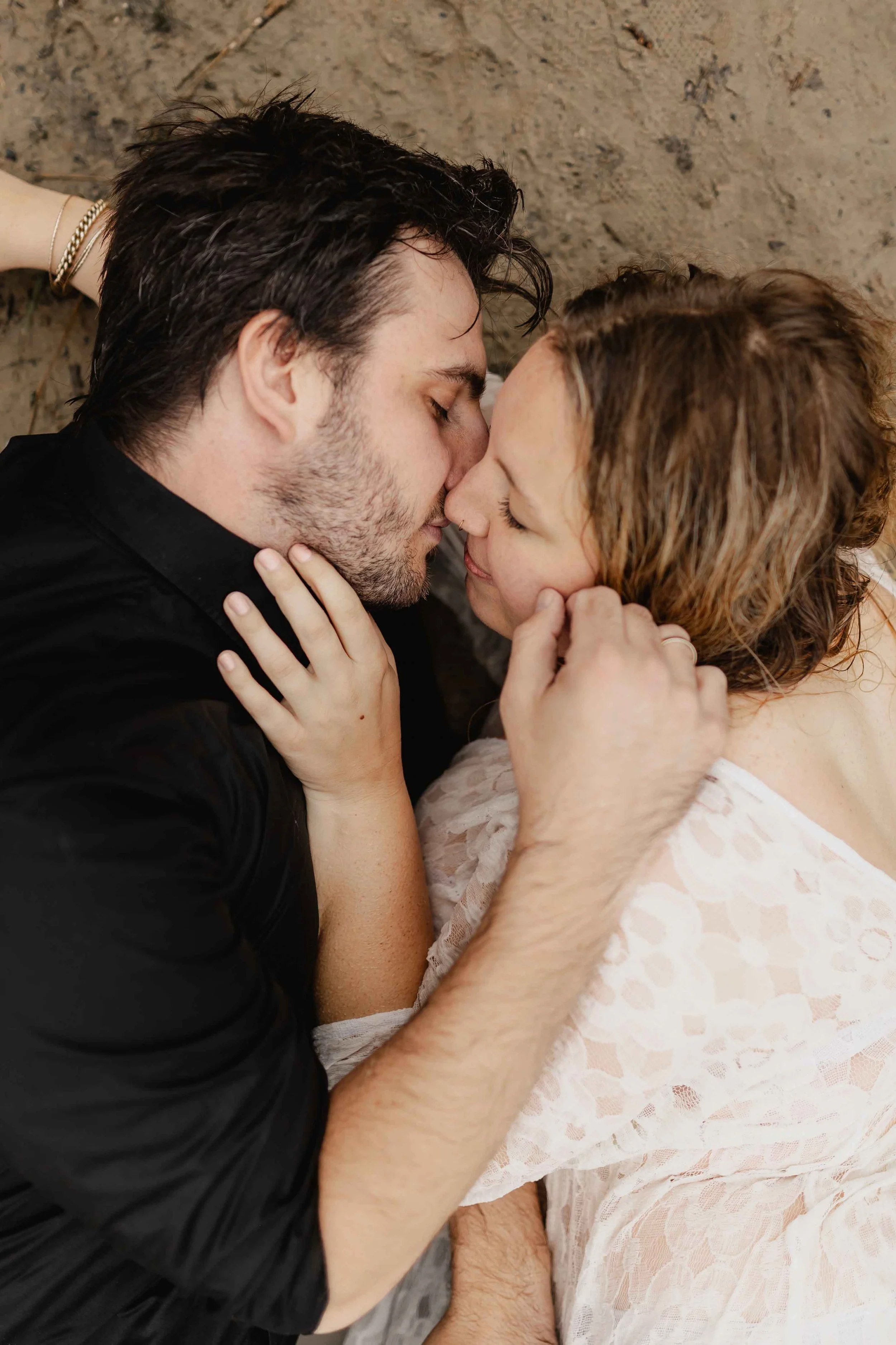 Paar liegt am Ufer und küsst sich leidenschaftlich, beide berühren sich sanft im Gesicht