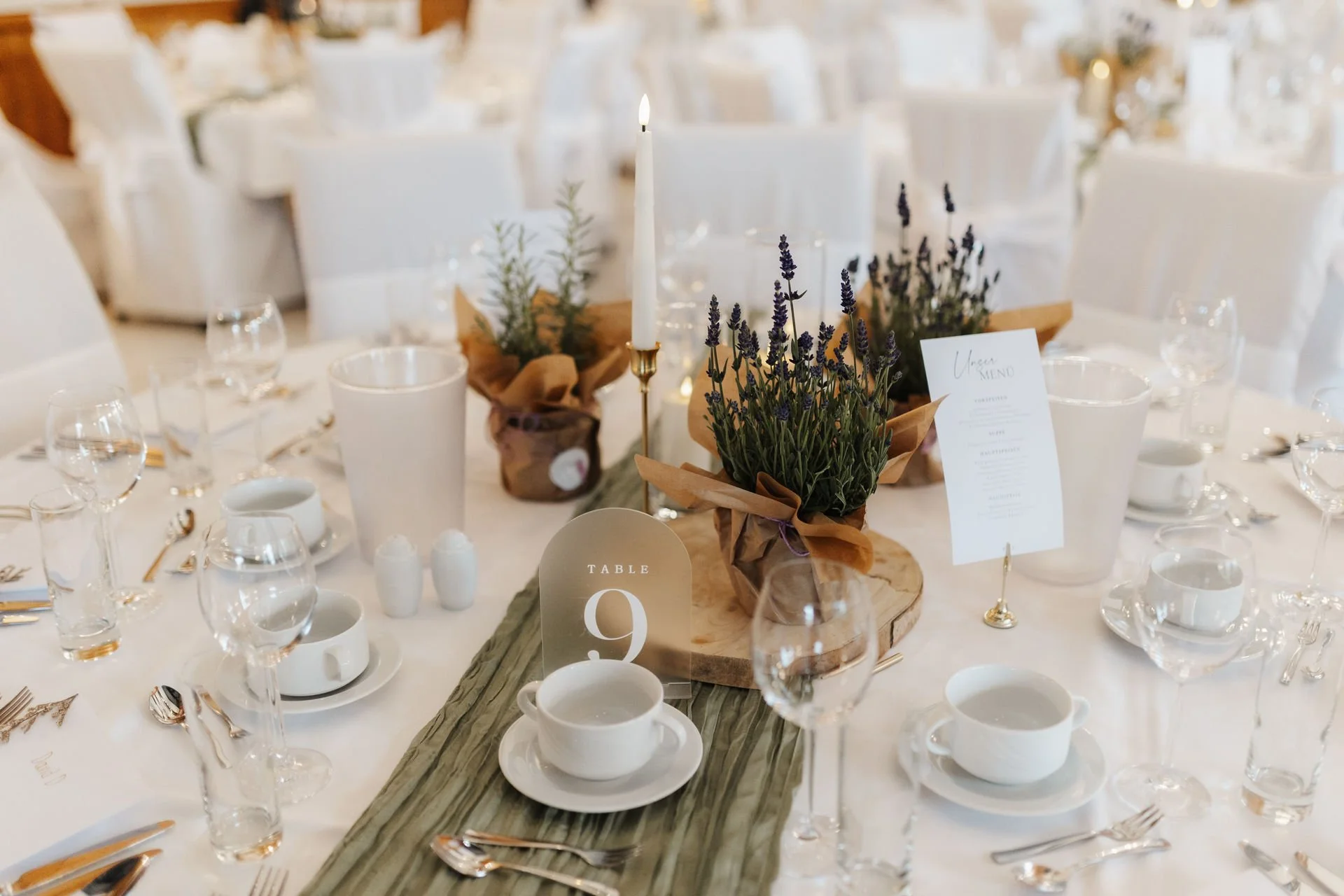 Liebevoll dekorierter Hochzeitstisch im Heide Hotel Reinstorf bei Lüneburg mit Lavendel, Kerzen, rustikalen Holzelementen und grünen Tischläufern.