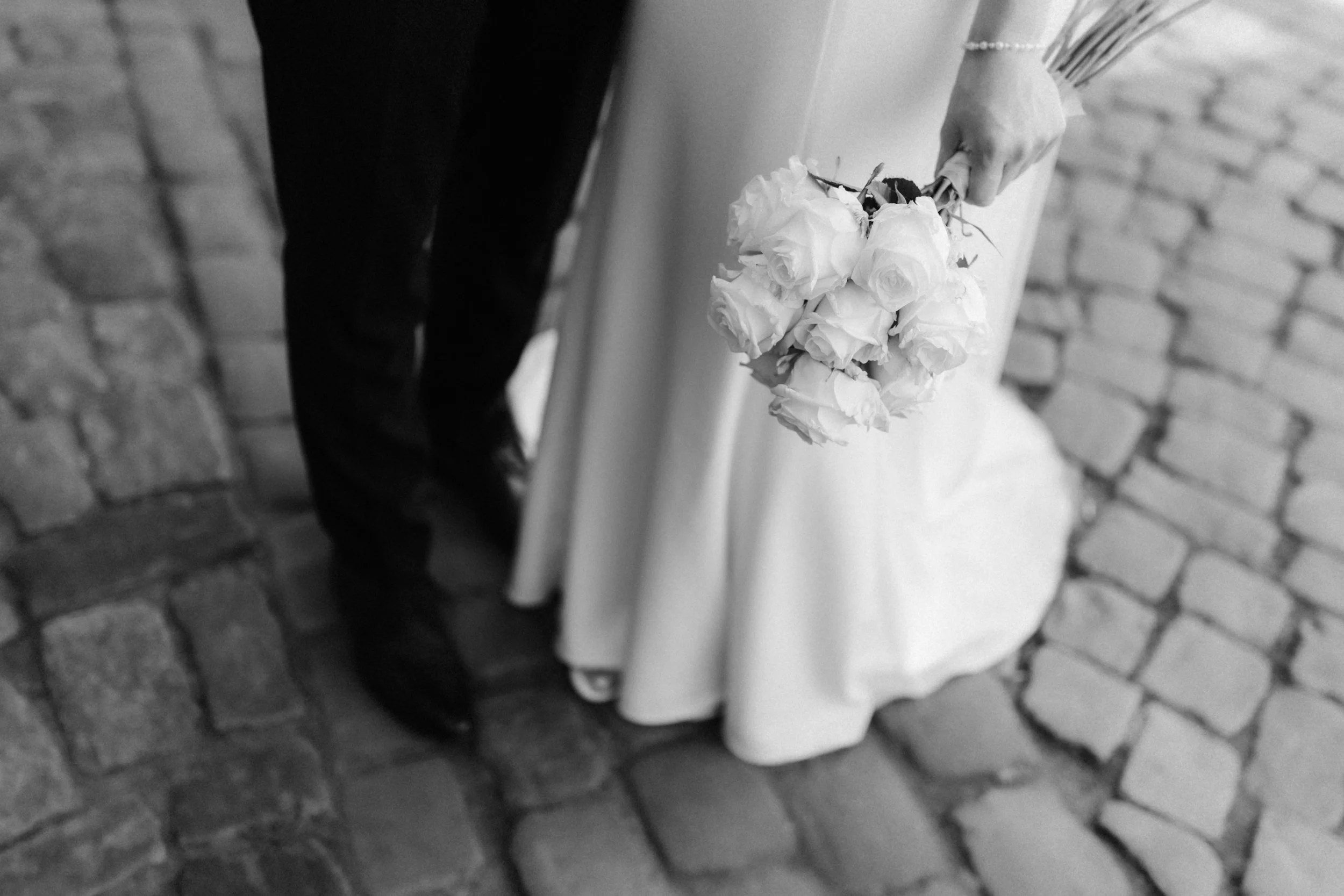 Schwarz-Weiß-Detailaufnahme des Brautstraußes und der Hochzeitskleidung eines Brautpaares in Lüneburg.