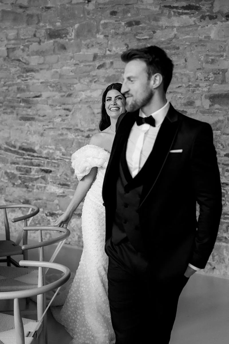 Elegantes Brautpaar bei einer modernen Hochzeit, stilvoll fotografiert in Schwarz-Weiß vor einer historischen Steinwand