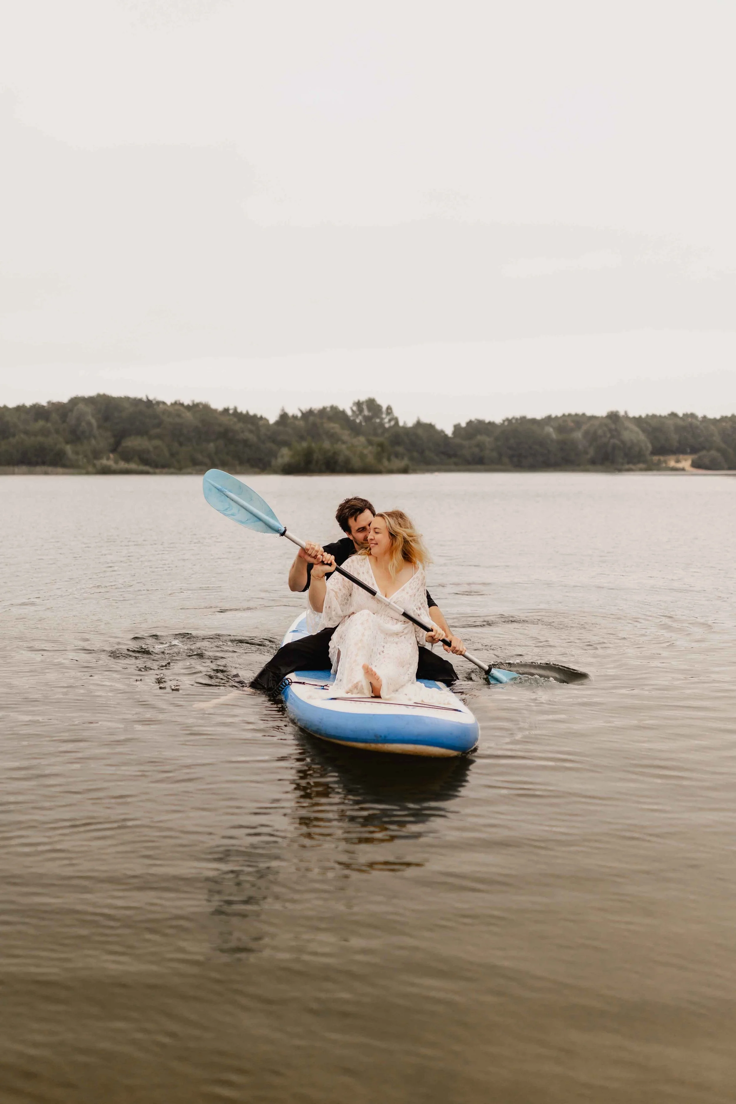 Paar fährt zusammen auf einem SUP-Board über den See und hält beim Paddeln eng zueinander