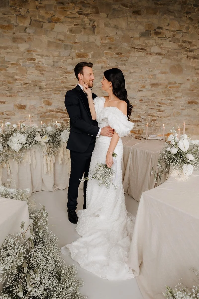 Brautpaar bei einer eleganten Hochzeit vor einer rustikalen Steinwand mit weißer Blumendekoration