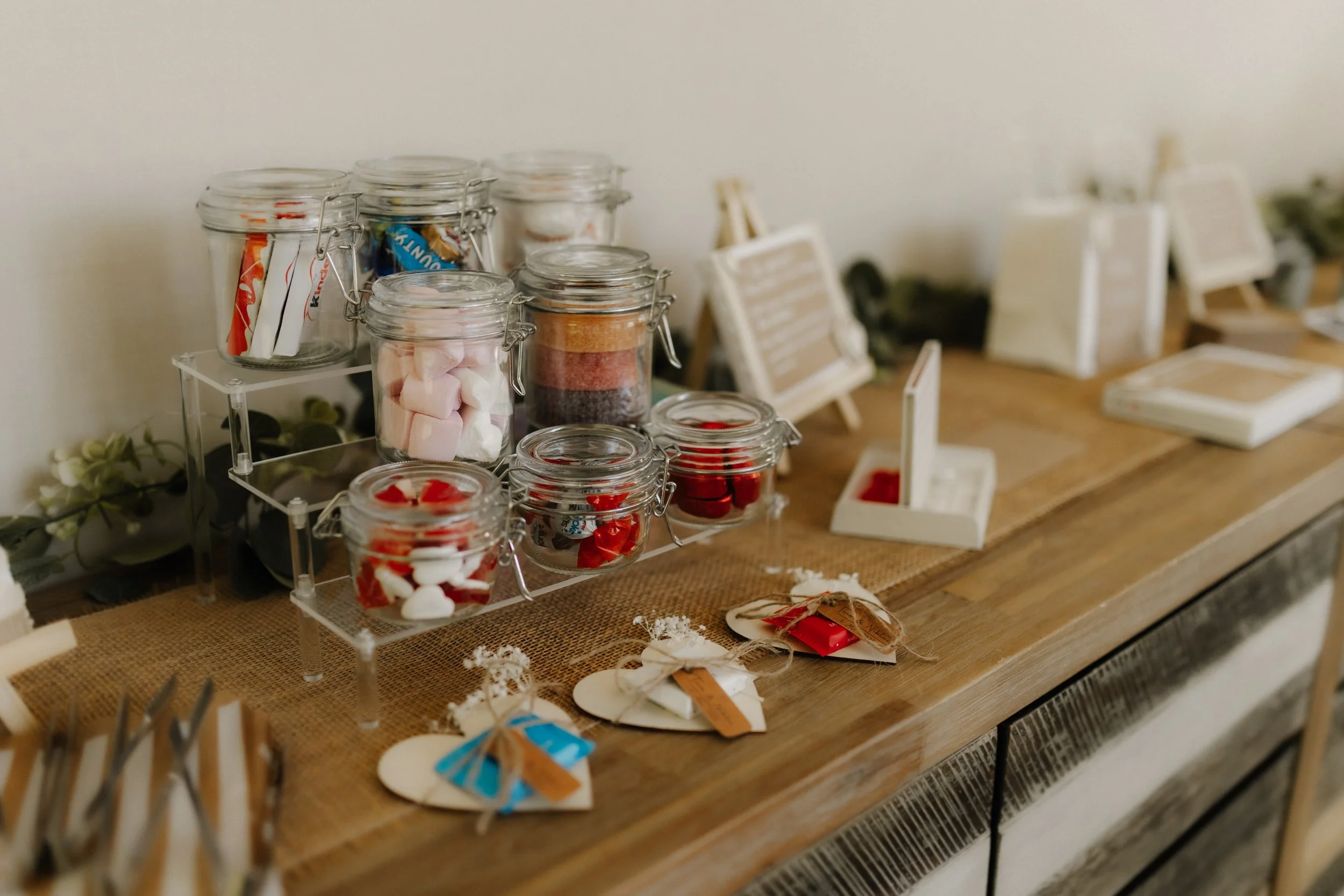 Liebevoll gestaltete Candybar mit Süßigkeiten in Glasgefäßen und kleinen Gastgeschenken auf einem rustikalen Holztisch bei einer Hochzeit.