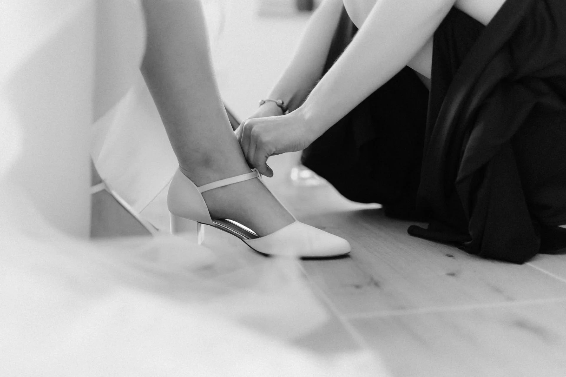Braut zieht sich vor der Hochzeit ihre weißen Brautschuhe an, fotografiert als Detailaufnahme in Schwarz-Weiß