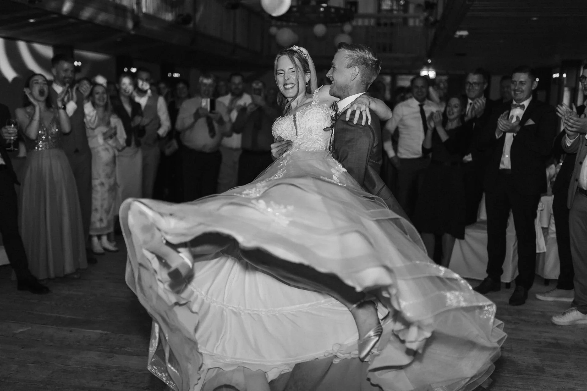 Brautpaar beim ausgelassenen Hochzeitstanz mit schwungvollem Brautkleid und jubelnden Gästen im Heide Hotel Reinstorf bei Lüneburg.
