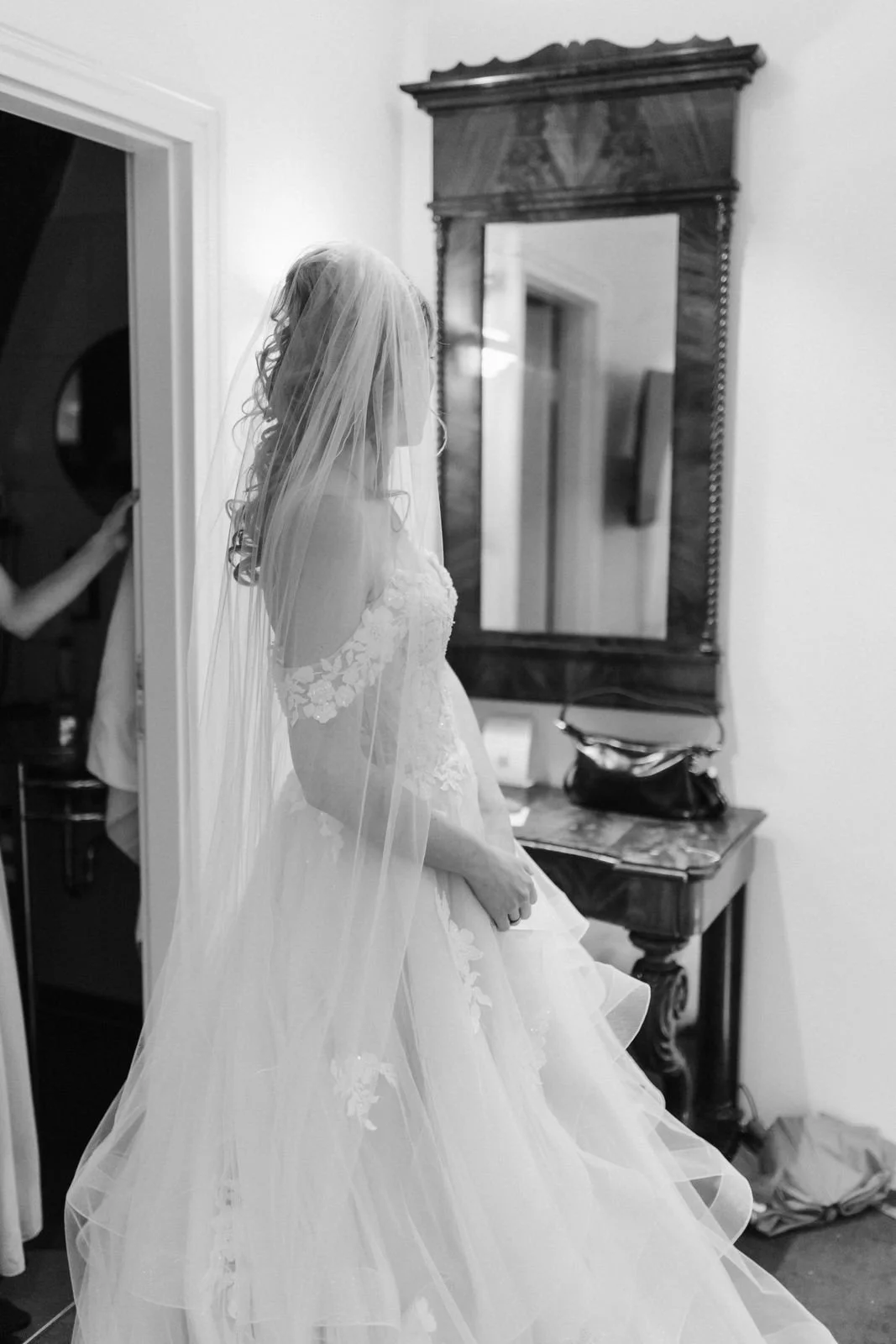 Schwarz-Weiß-Aufnahme einer Braut im Hochzeitskleid mit langem Schleier beim Getting Ready vor einem antiken Spiegel im Heide Hotel Reinstorf bei Lüneburg.