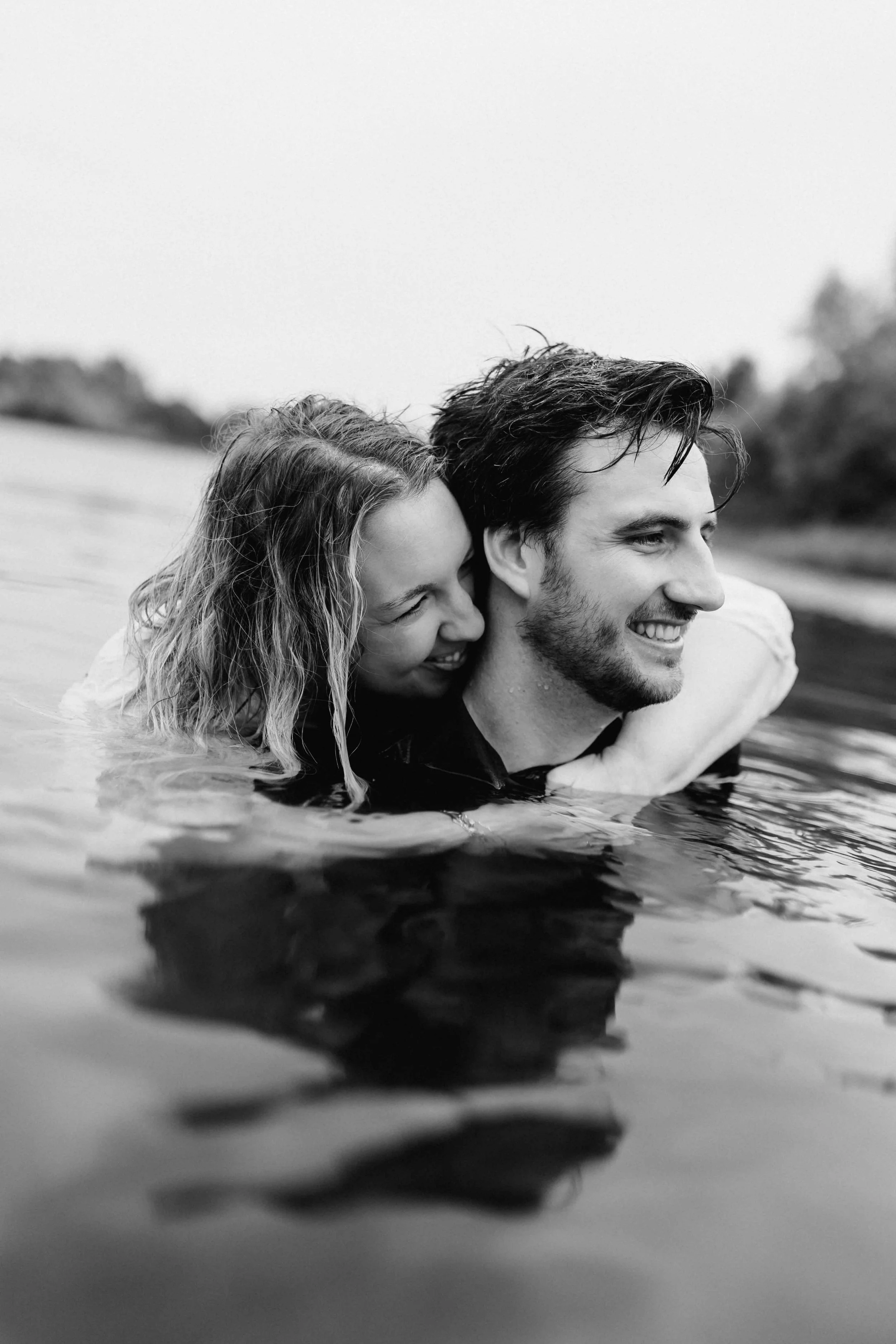 Frau umarmt ihren Partner von hinten im Wasser, beide lachen glücklich