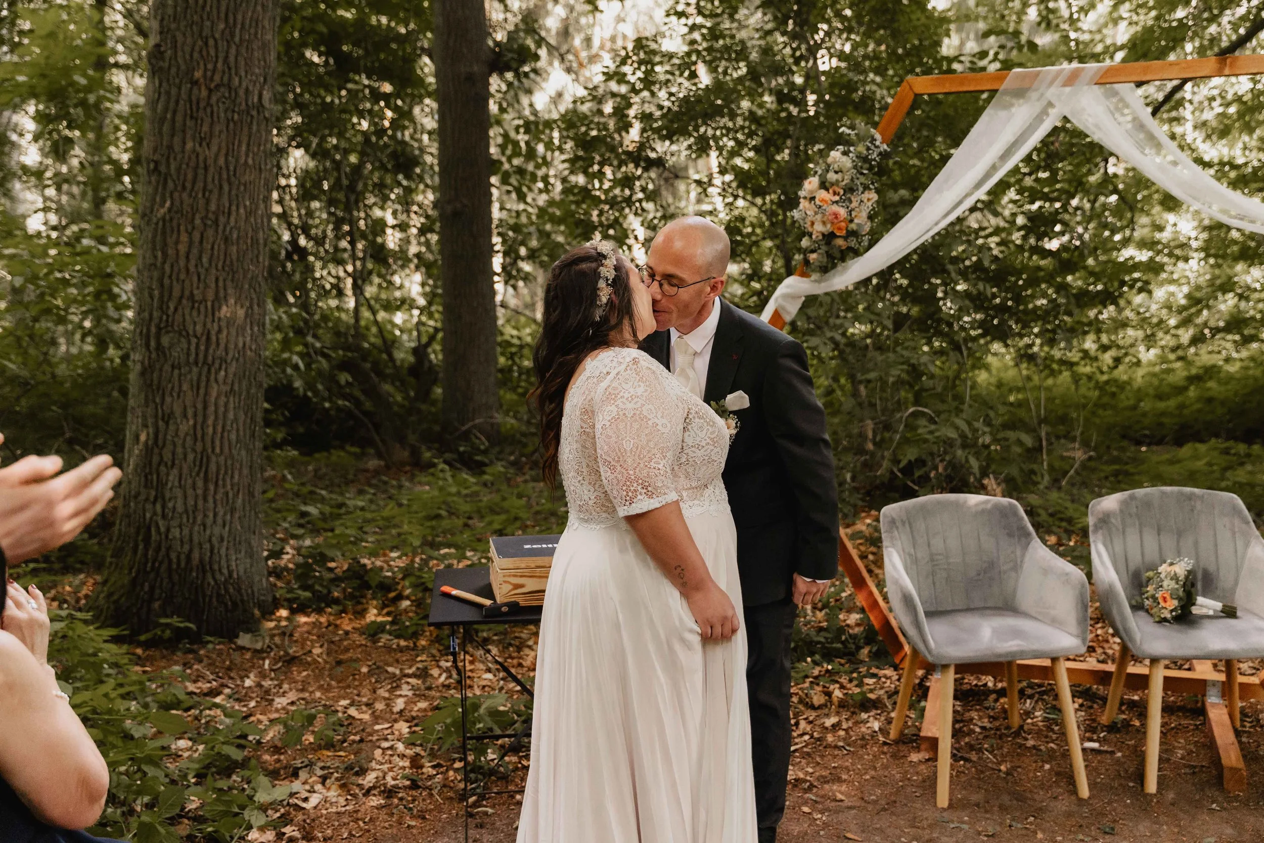 Hochzeitspaar küsst sich nach dem Trauritual unter einem Blumenbogen im Wald