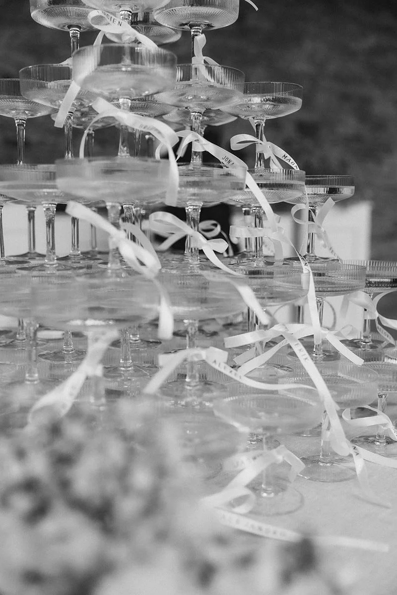 Schwarz-Weiß-Aufnahme eines Champagnerturms aus zahlreichen Gläsern, dekoriert mit weißen Schleifen für eine elegante Hochzeitsfeier
