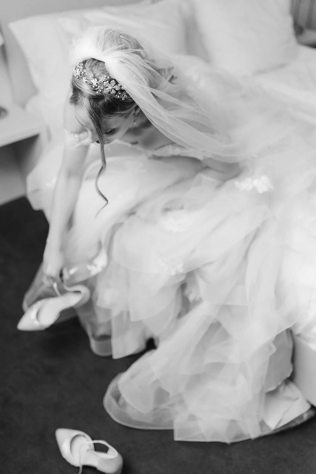 Schwarz-Weiß-Aufnahme der Braut beim Anziehen ihrer Brautschuhe, umgeben von den zarten Tülllagen ihres Hochzeitskleides und ihrem Schleier – authentisches Getting Ready im Heide Hotel Reinstorf bei Lüneburg.