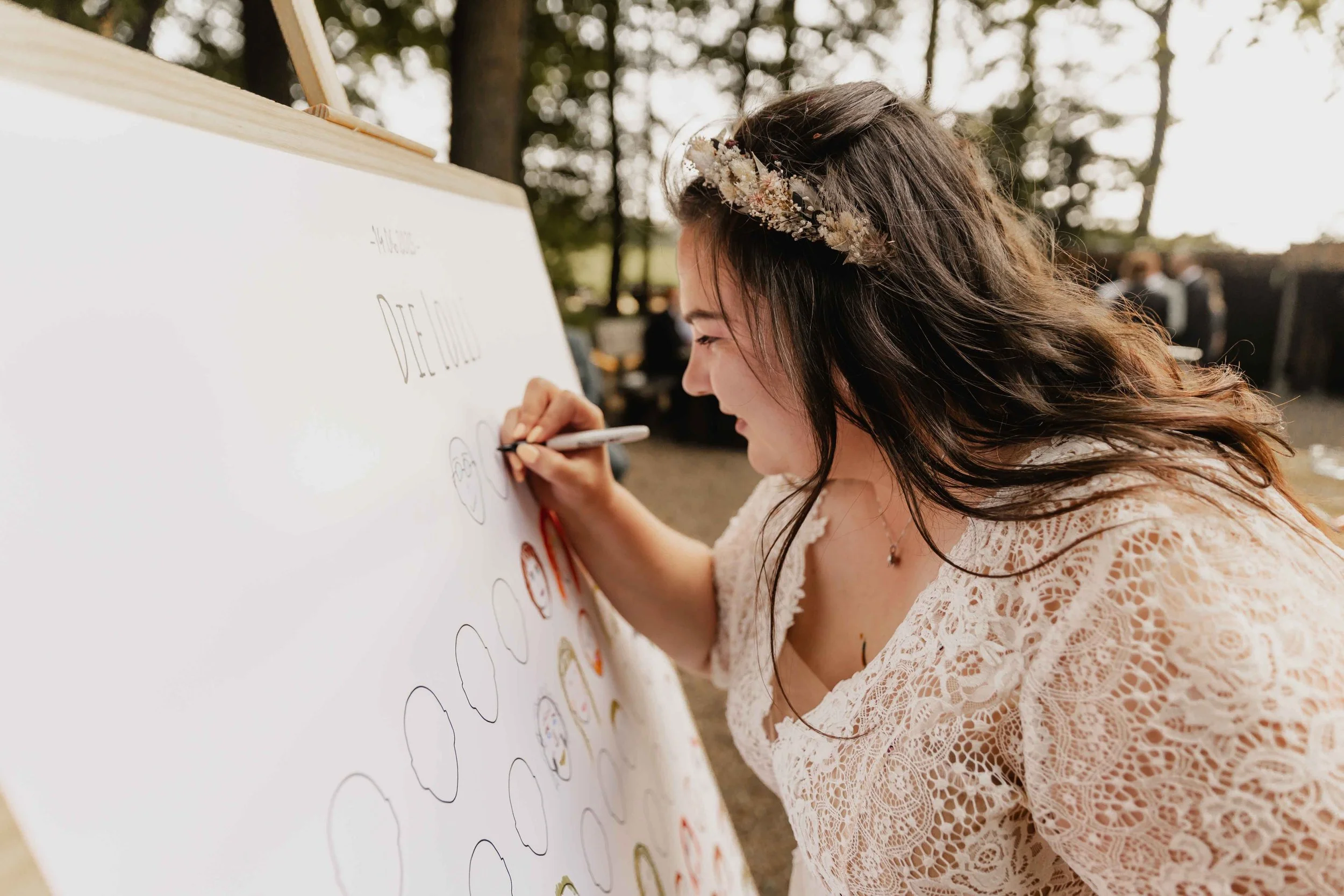 Braut malt mit einem Filzstift ein Gesicht auf das Gästeporträt bei der Hochzeit