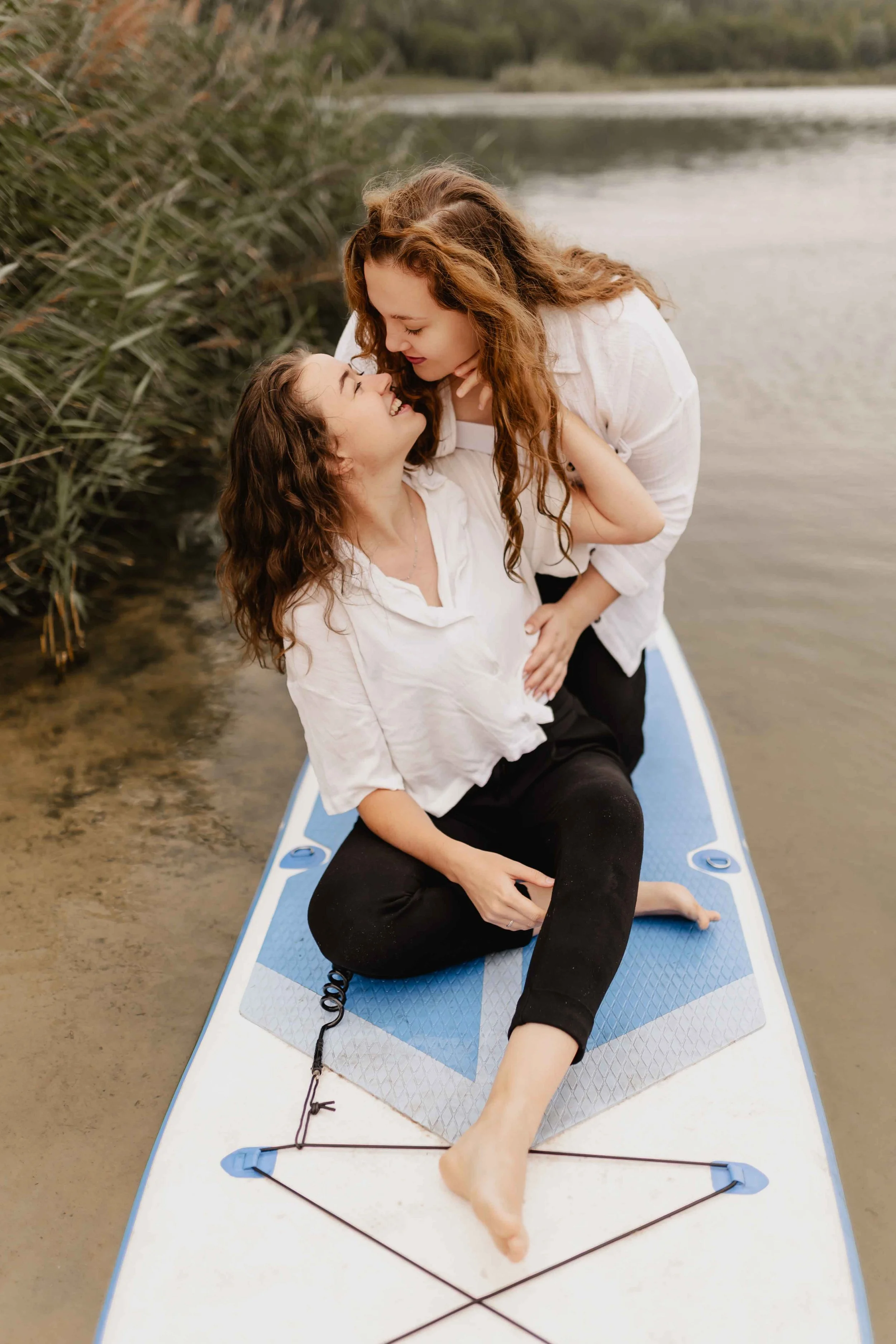 Zwei Frauen sitzen auf einem SUP-Board, schauen sich tief in die Augen und genießen den romantischen Moment