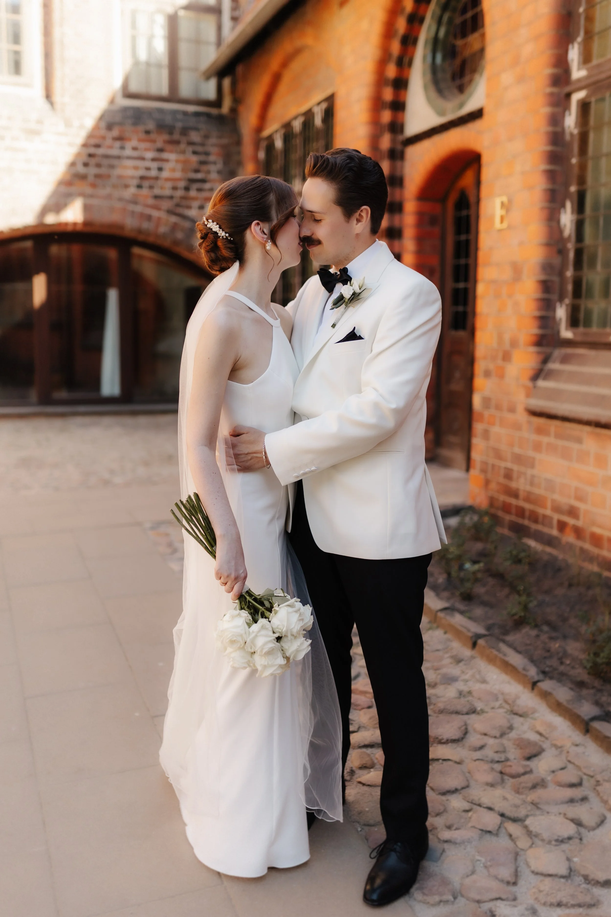 Brautpaar küsst sich nach seiner Hochzeit im Rathausgarten in Lüneburg, die Braut hält einen weißen Brautstrauß in der Hand.