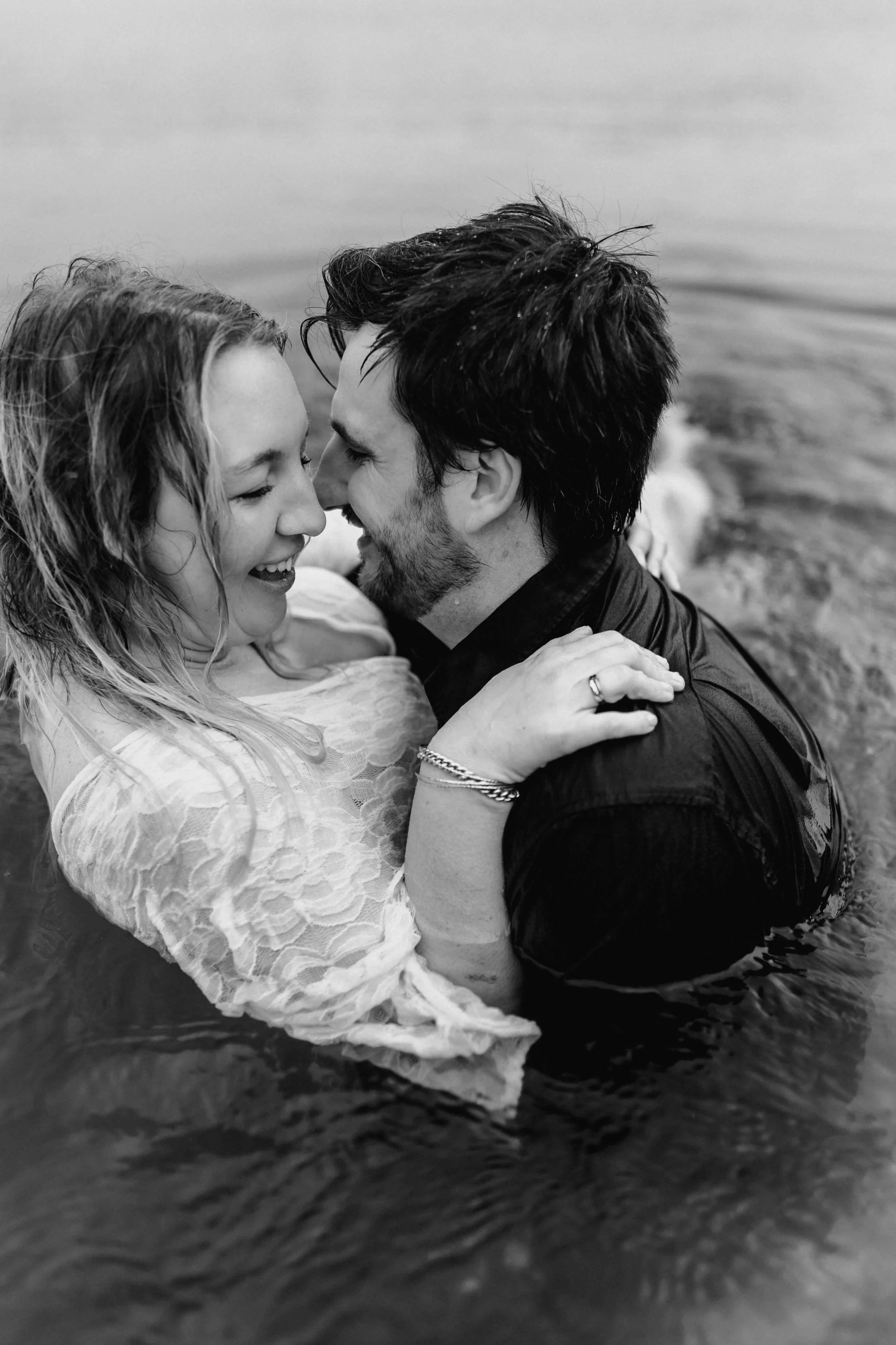 Paar steht im Wasser, umarmt sich eng und lacht sich verliebt an