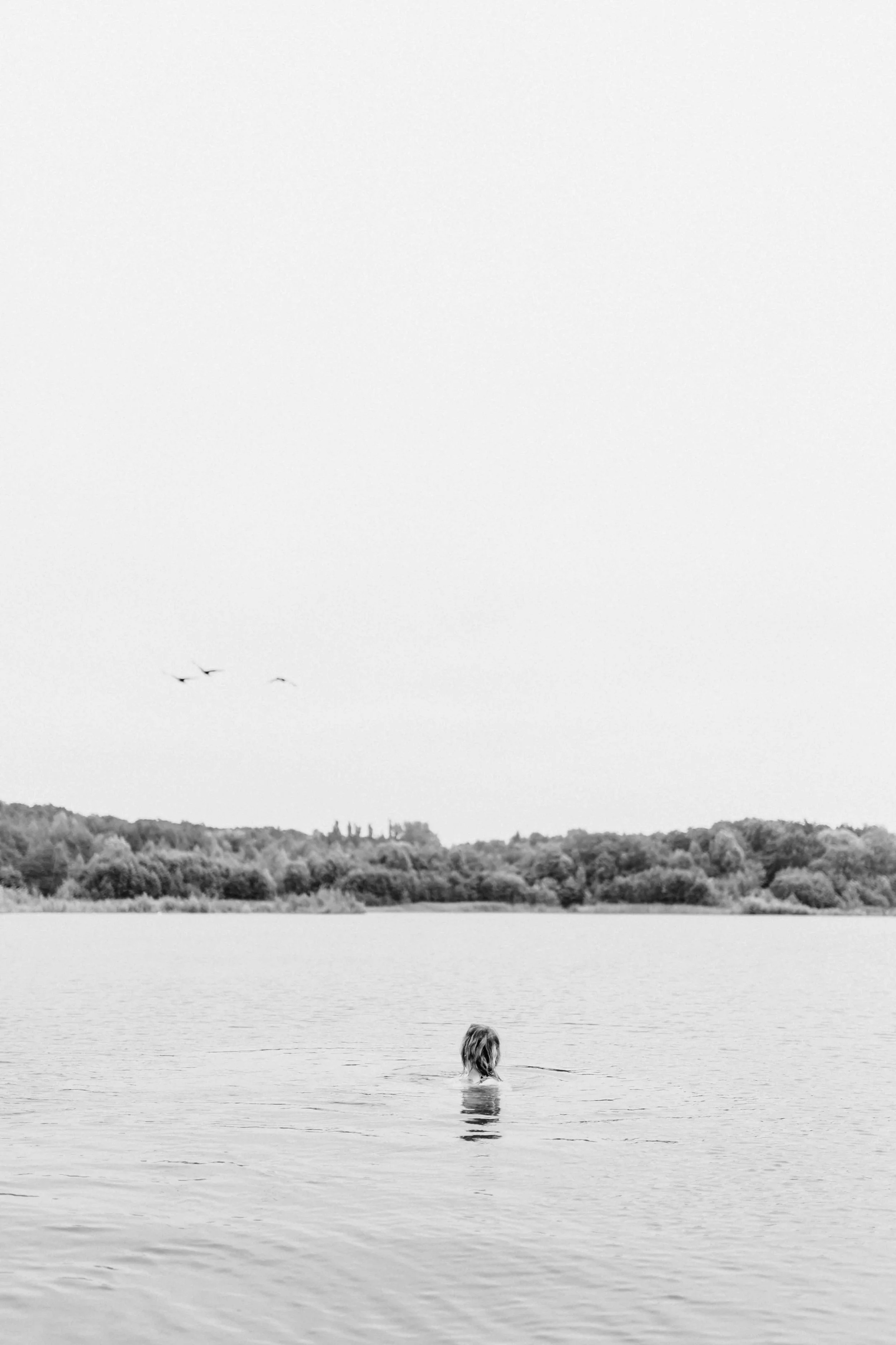Weitwinkelaufnahme von einer Frau im See, klein im Bild und umgeben von viel Wasser und Natur