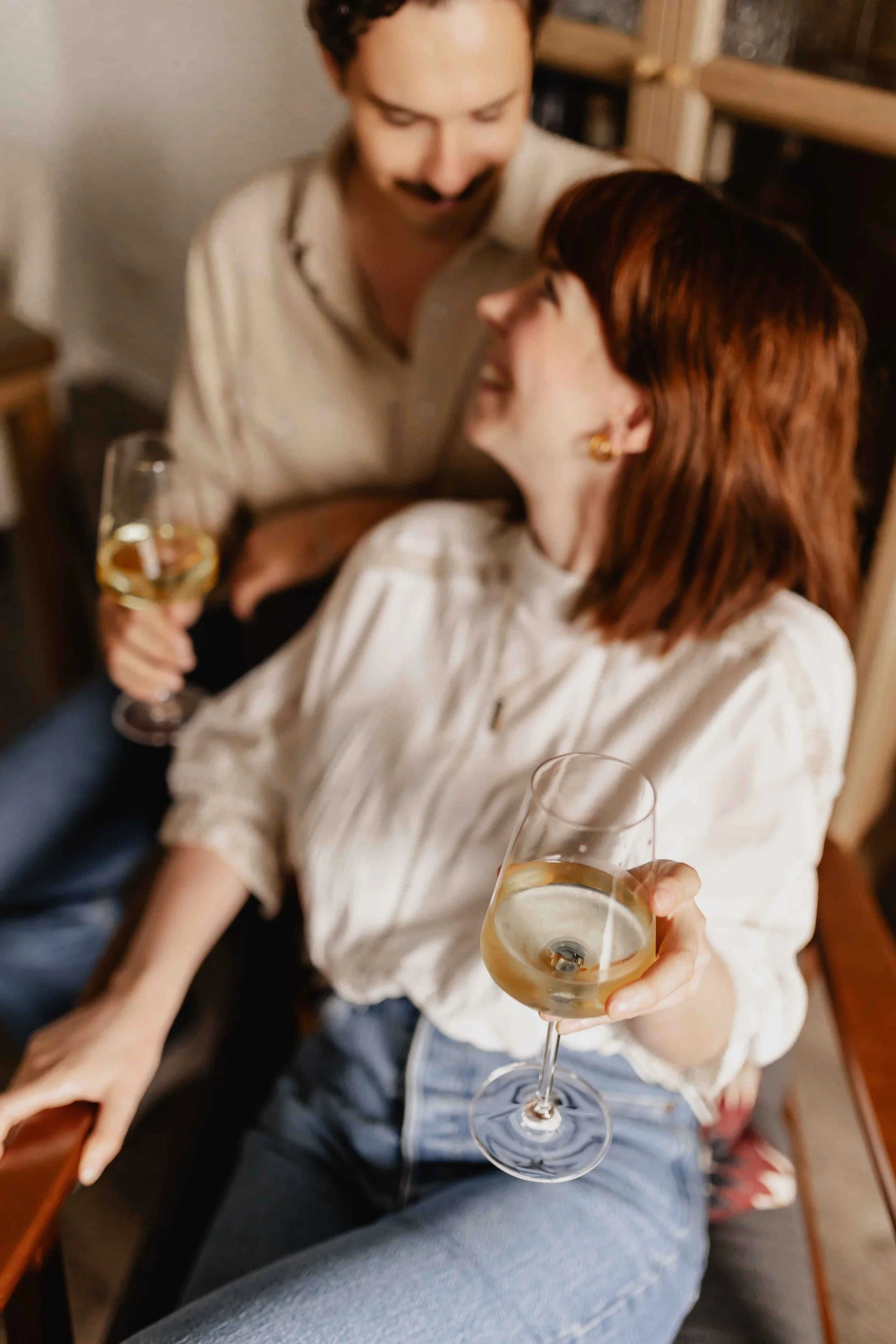 Paar bei einer Homestory in Lüneburg sitzt eng beieinander, hält Gläser mit Wein und schaut sich lächelnd an