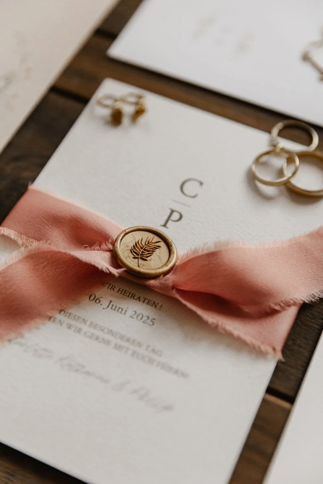 Hochzeitseinladung mit goldfarbenem Wachssiegel, rosa Seidenschleife und Trauringen als stilvolles Hochzeitsdetail in Lüneburg