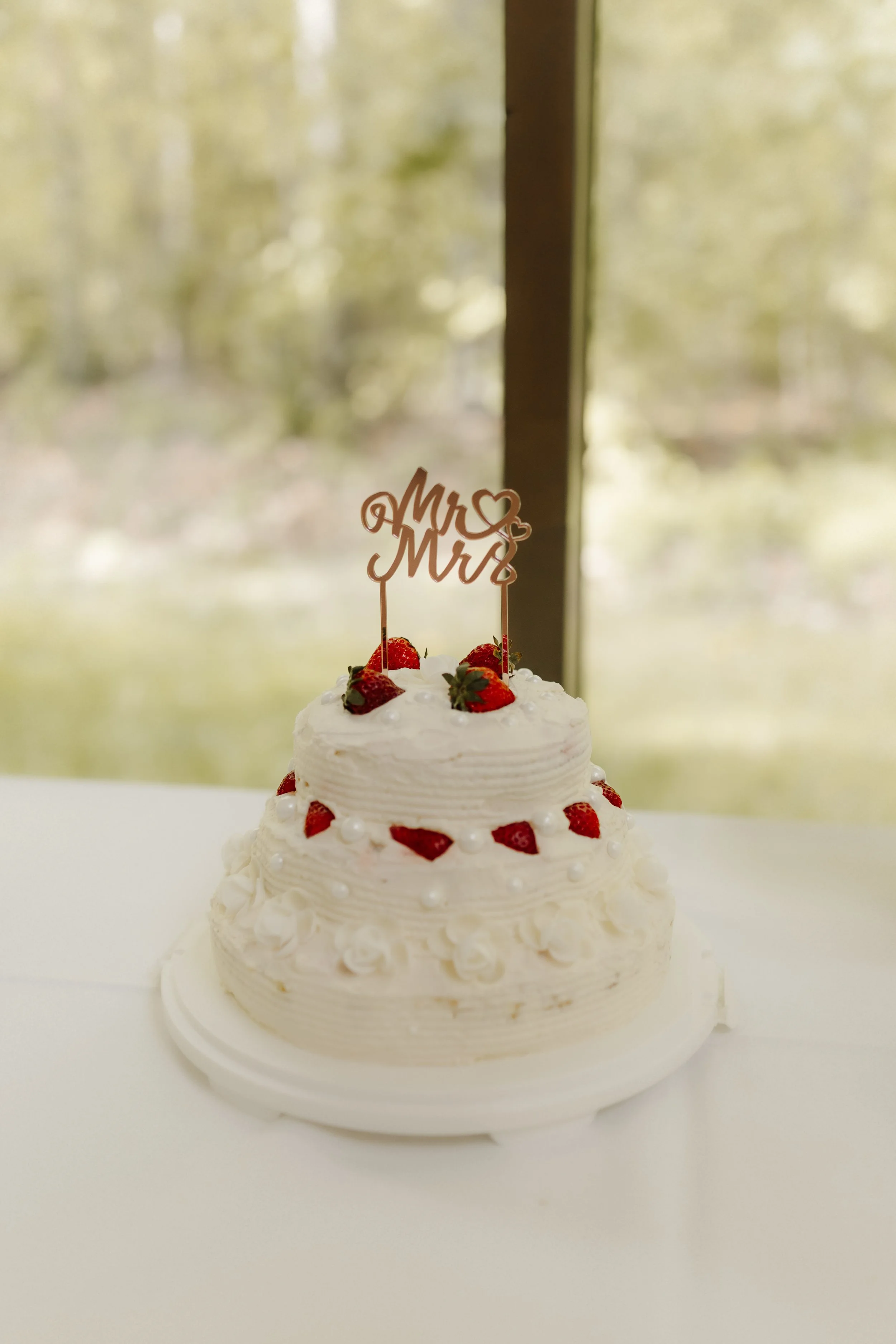 Zweistöckige weiße Hochzeitstorte mit Erdbeeren und einem Mr & Mrs Cake Topper bei einer Hochzeitsfeier im Forsthaus Rote Schleuse in Lüneburg.
