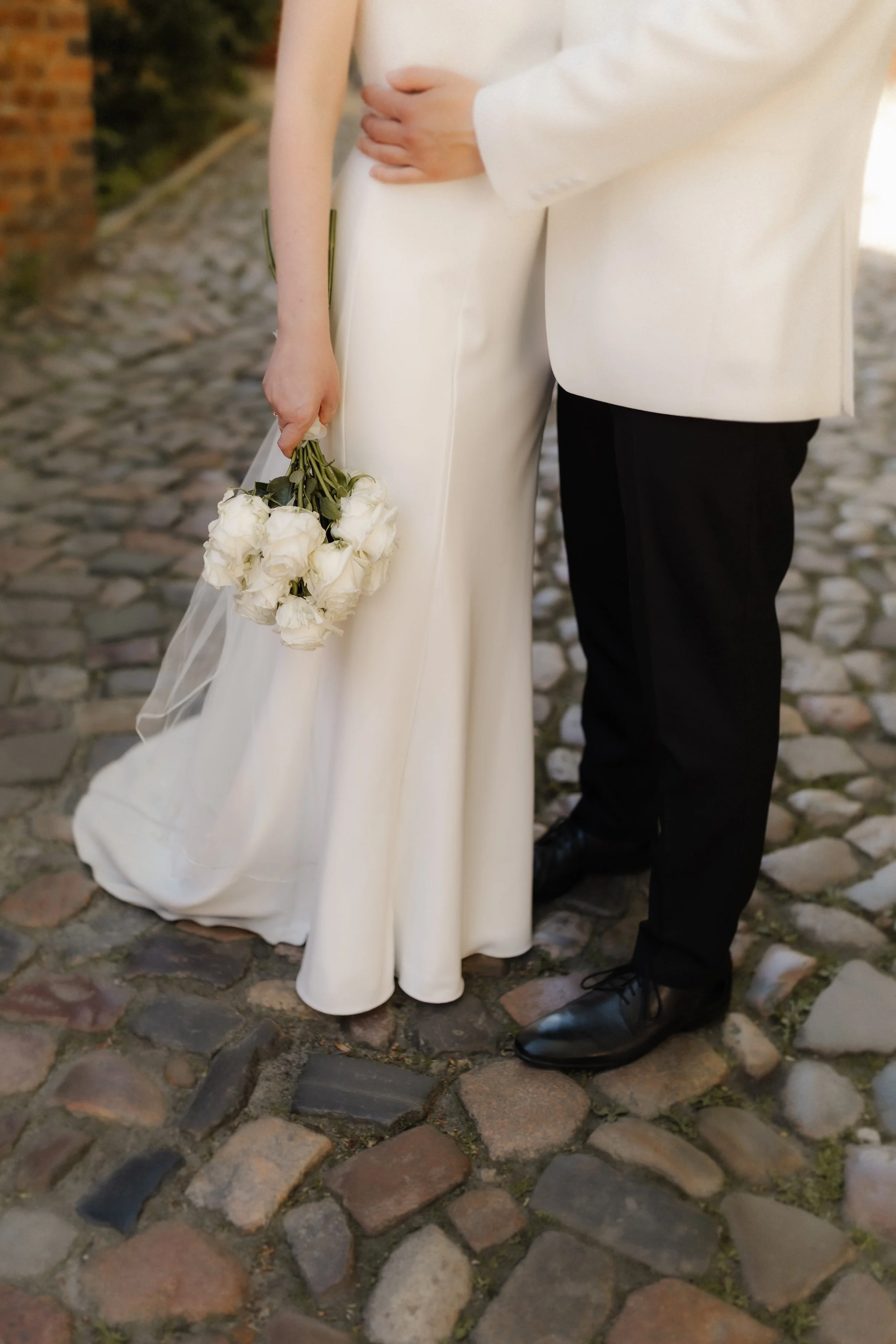Detailaufnahme eines Brautpaares mit weißem Brautkleid, weißem Brautstrauß und elegantem Hochzeitsanzug in Lüneburg.