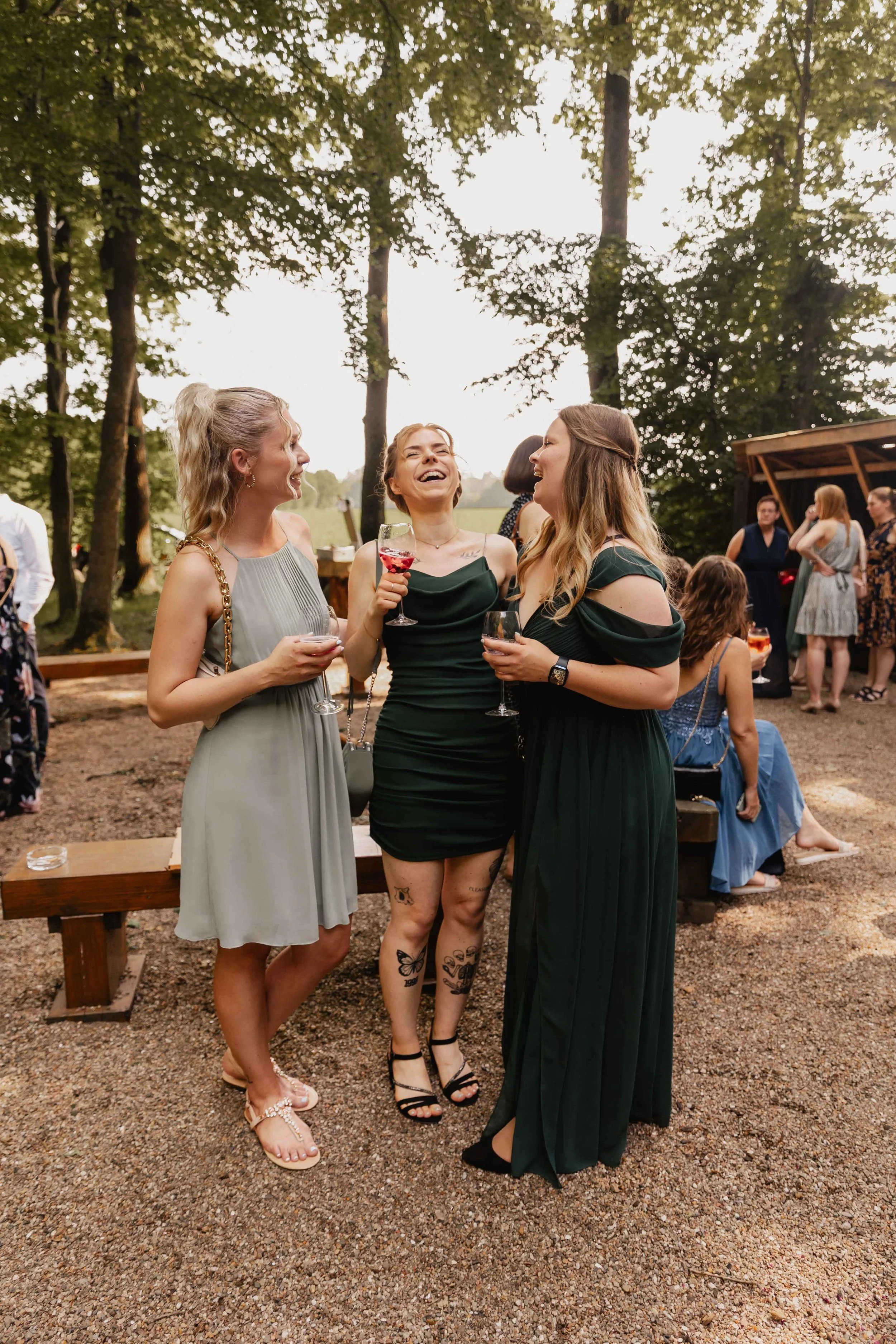Drei Frauen in Sommerkleidern lachen herzlich mit Weingläsern in der Hand